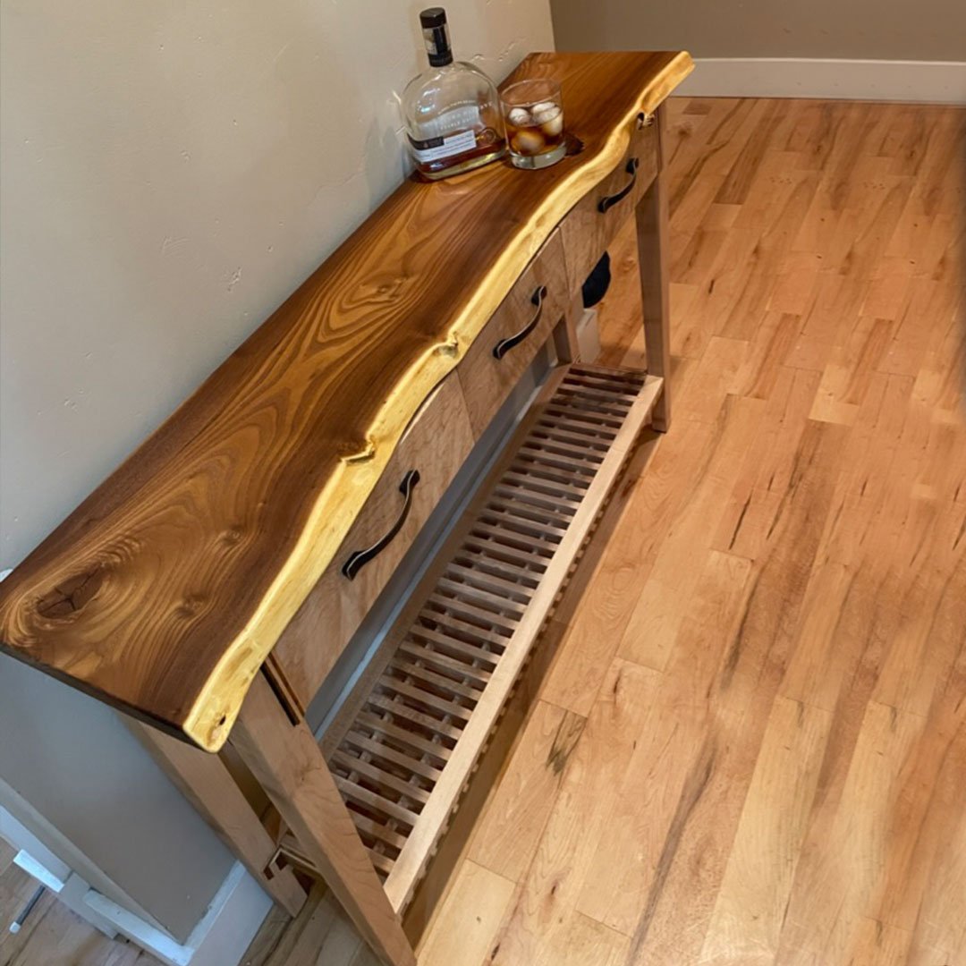 An entry table made for family. Three drawers with very colorful insides. Russian olive wood live edge top. The base is fiddleback maple. 
