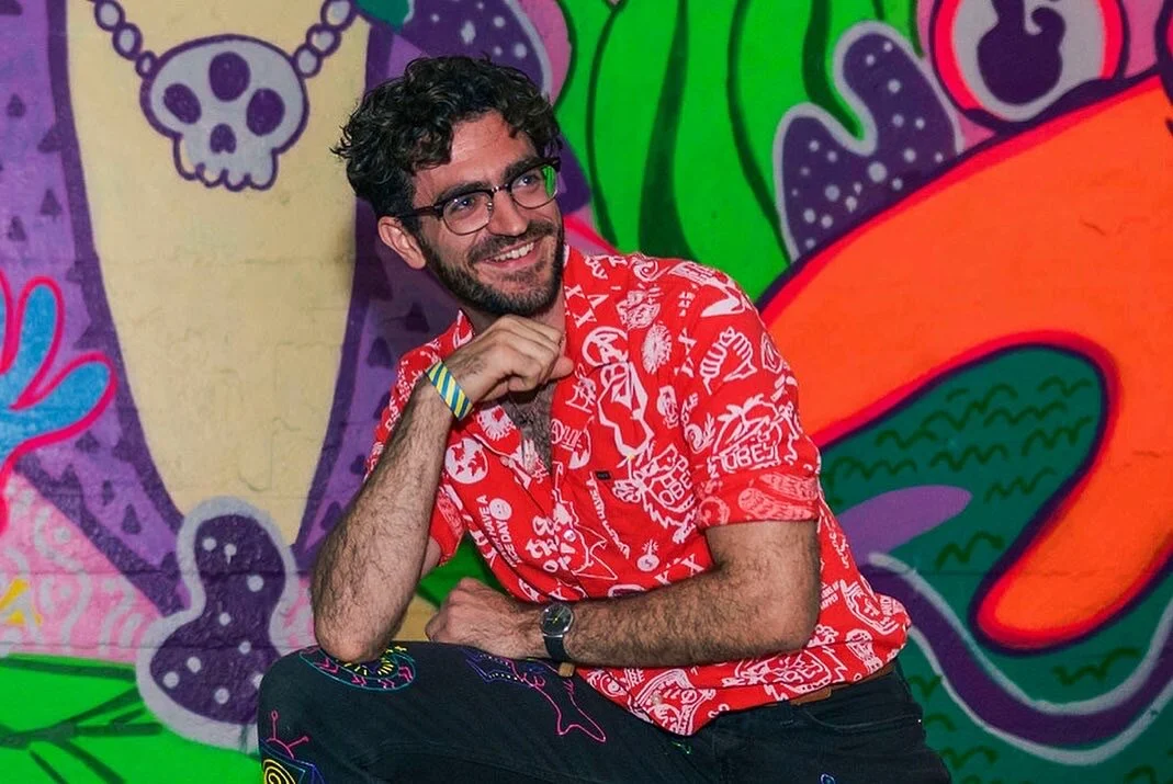 Man in red graphic shirt posing in front of colorful graffiti wall.