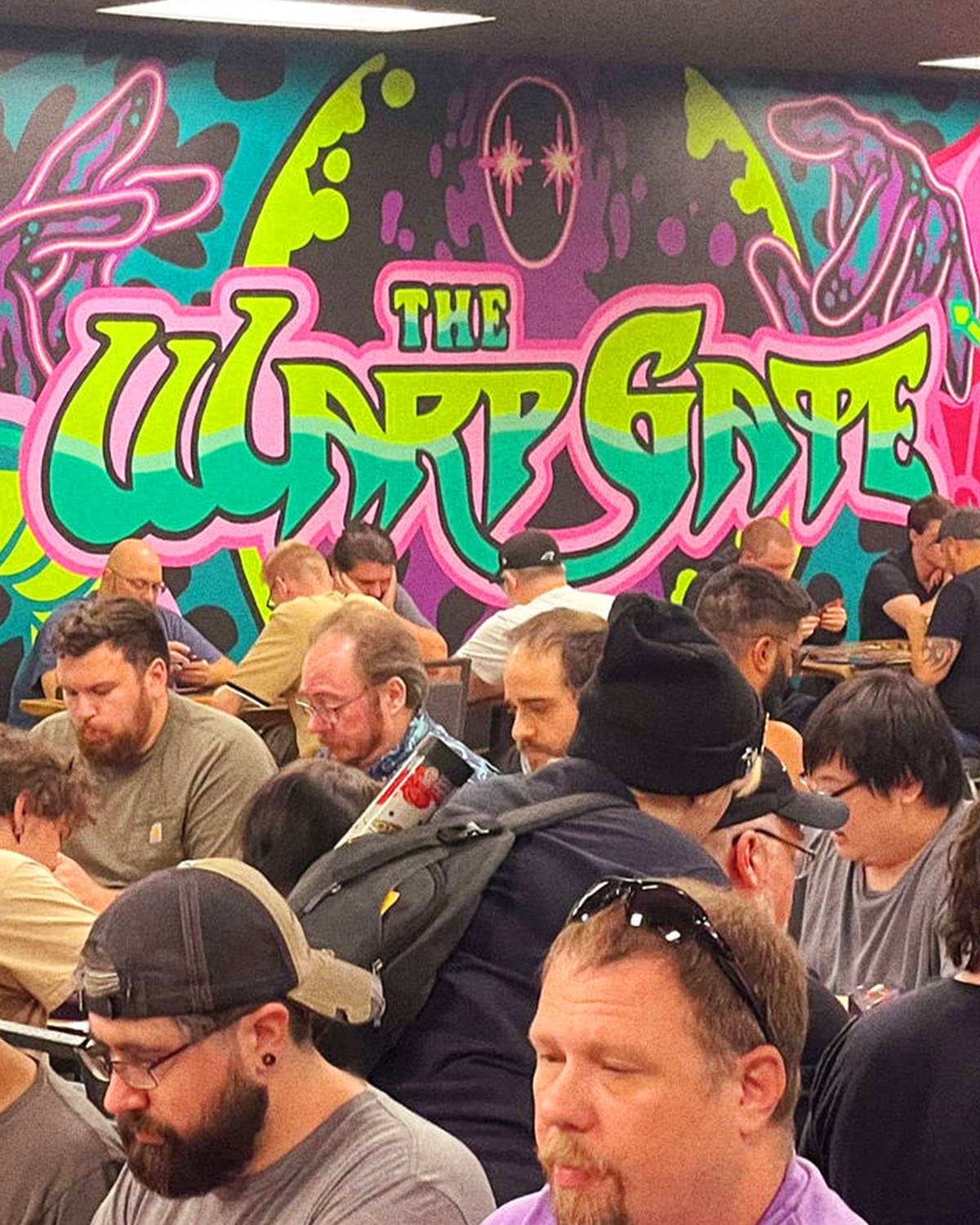 Graffiti-style Warp Gate mural in neon green, pink, and teal above a full gaming floor of card players in Columbus, Ohio.