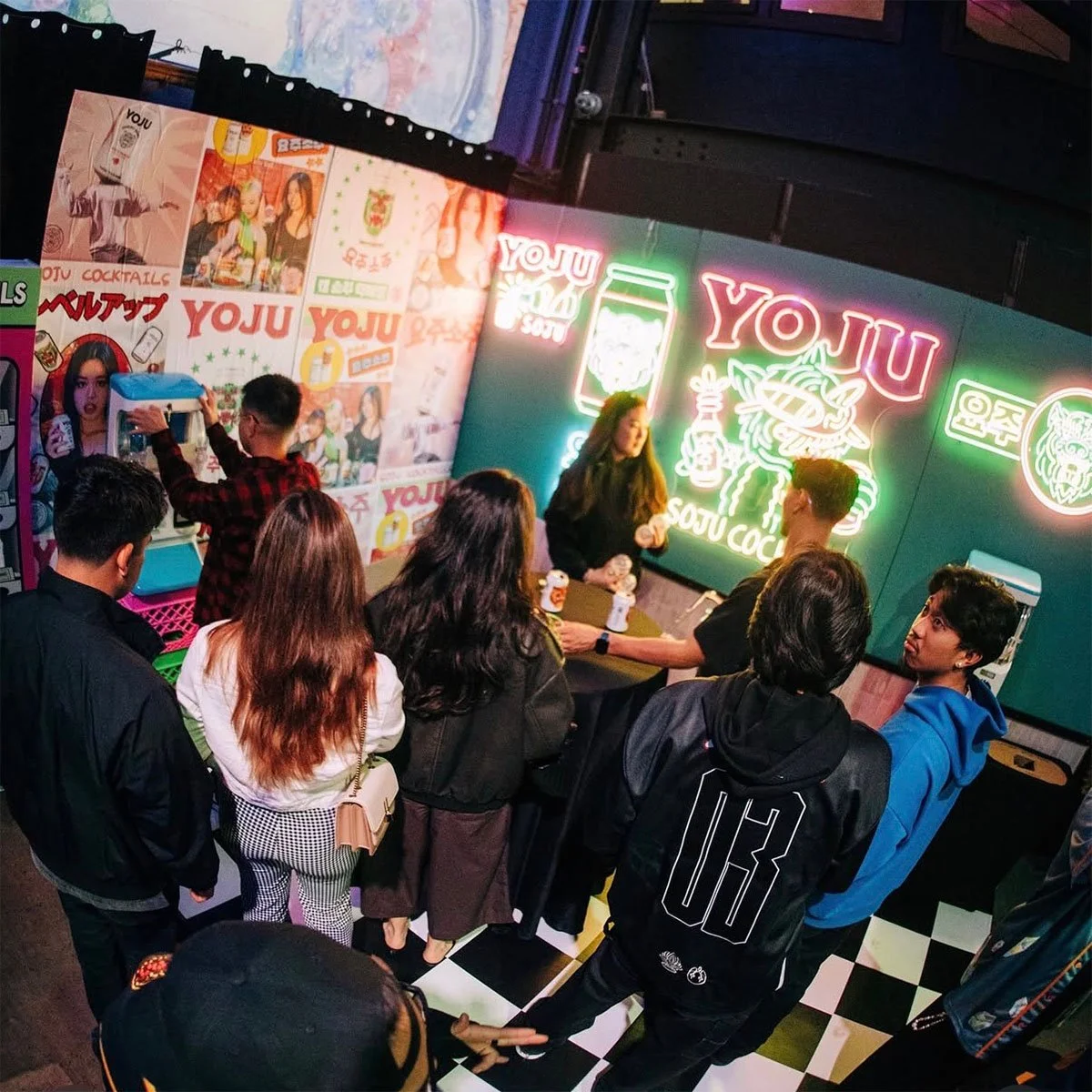 Guests gathered at the Yoju pocha-arcade pop-up at night, with the neon tiger wall and Korean poster wall lit behind them.