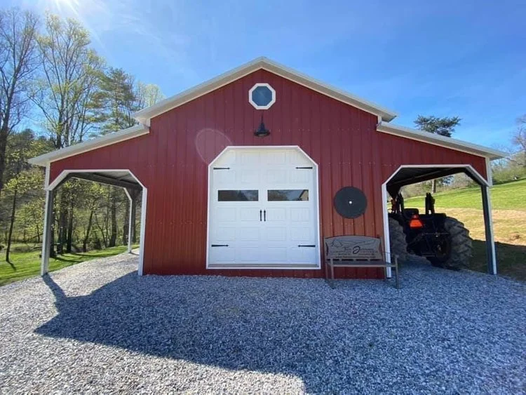 red metal barn with 2 shelters and large rollup door. A tractor us under one of the side shelter lean to.