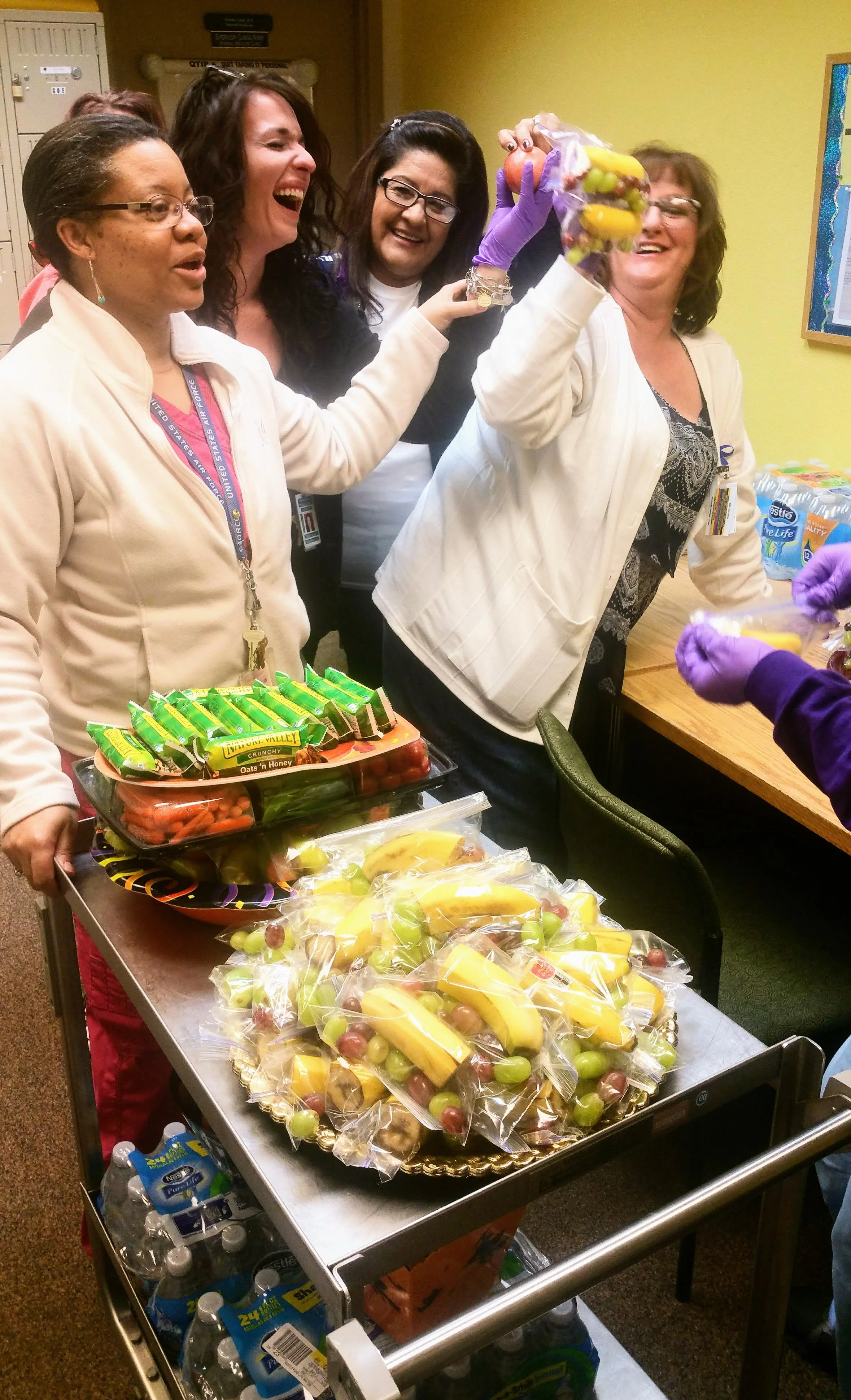 Group of women and staff preparing and sharing care packages with various fruits and snacks in an indoor setting.