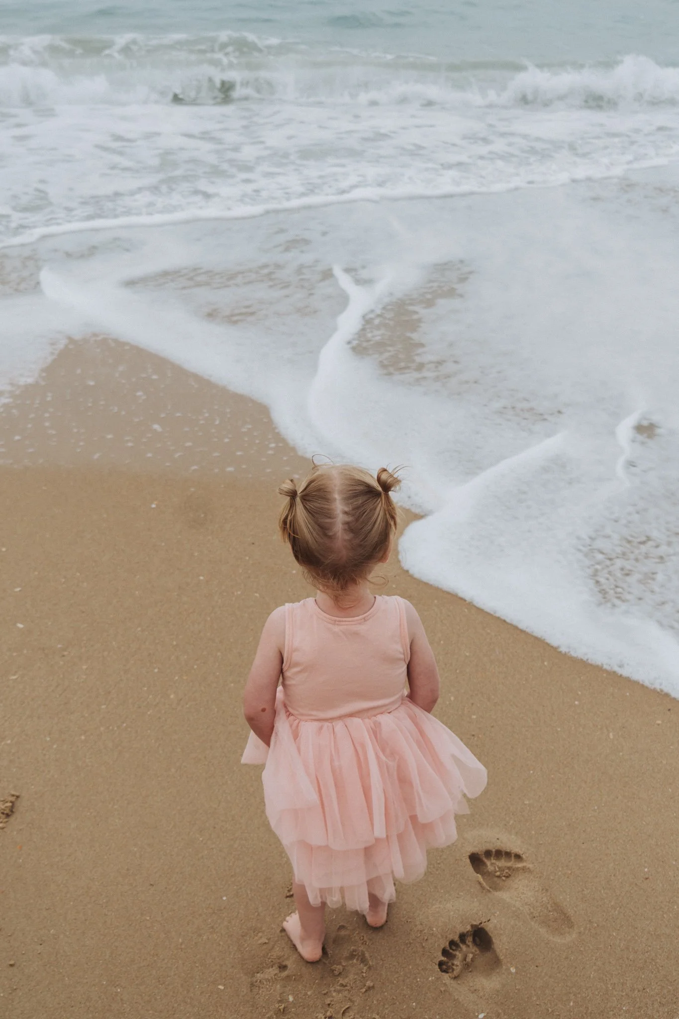 Photo of a little girl standing on the beach looking out to sea