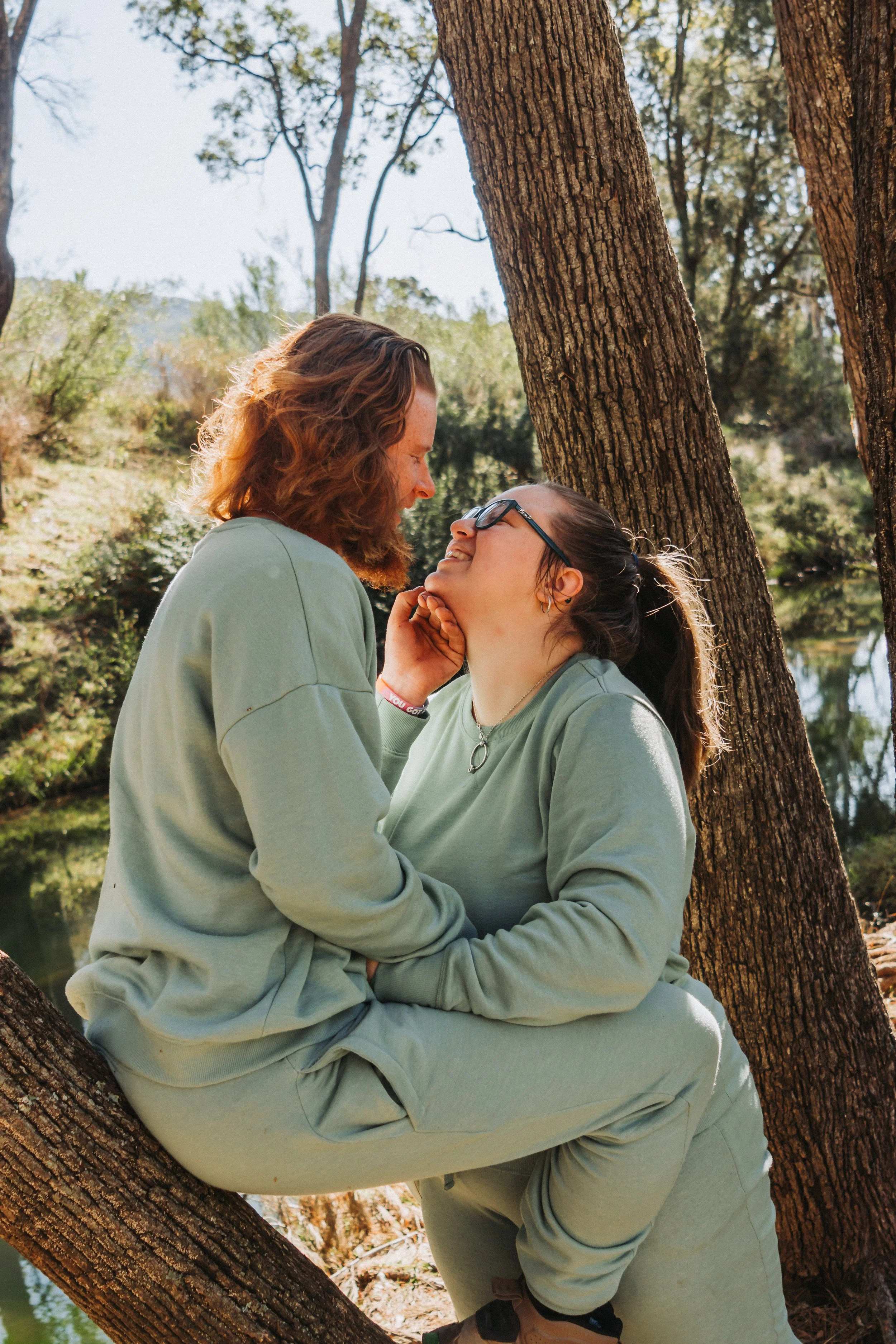 Young couple snuggling close between trees beside a creek