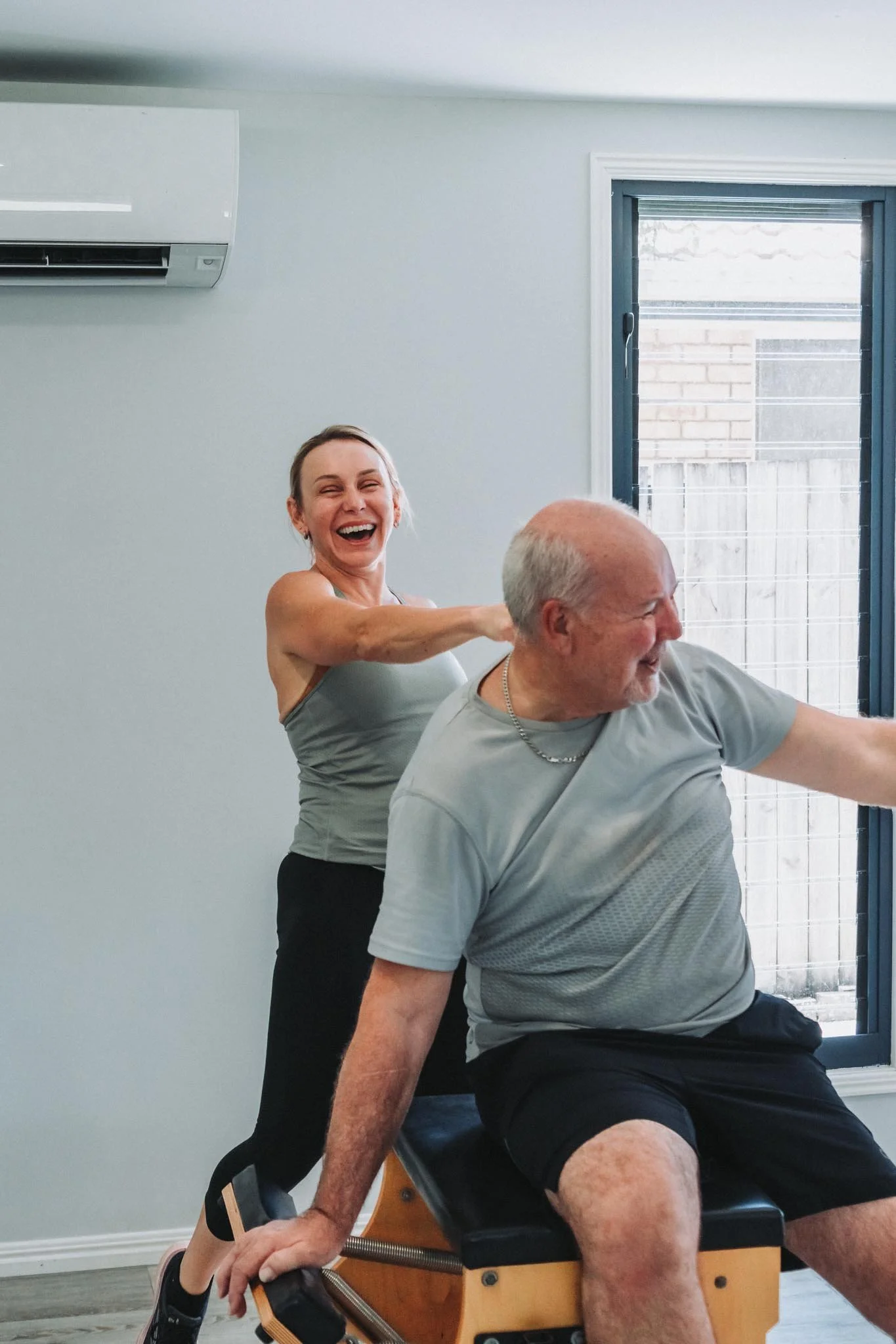 Mel adjusting a male client's movement through an exercise. Both mid belly laugh