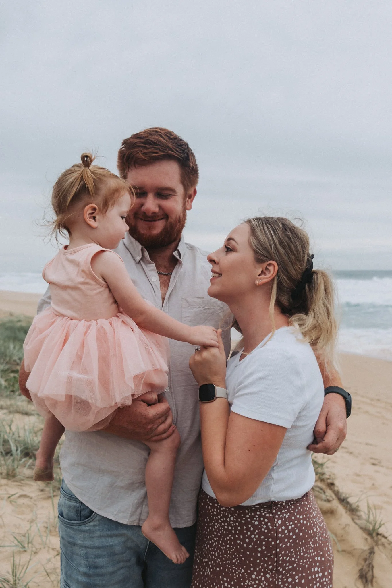 Young family of three snuggling and giggling together on Sunshine Coast's Beach Kawana Beach