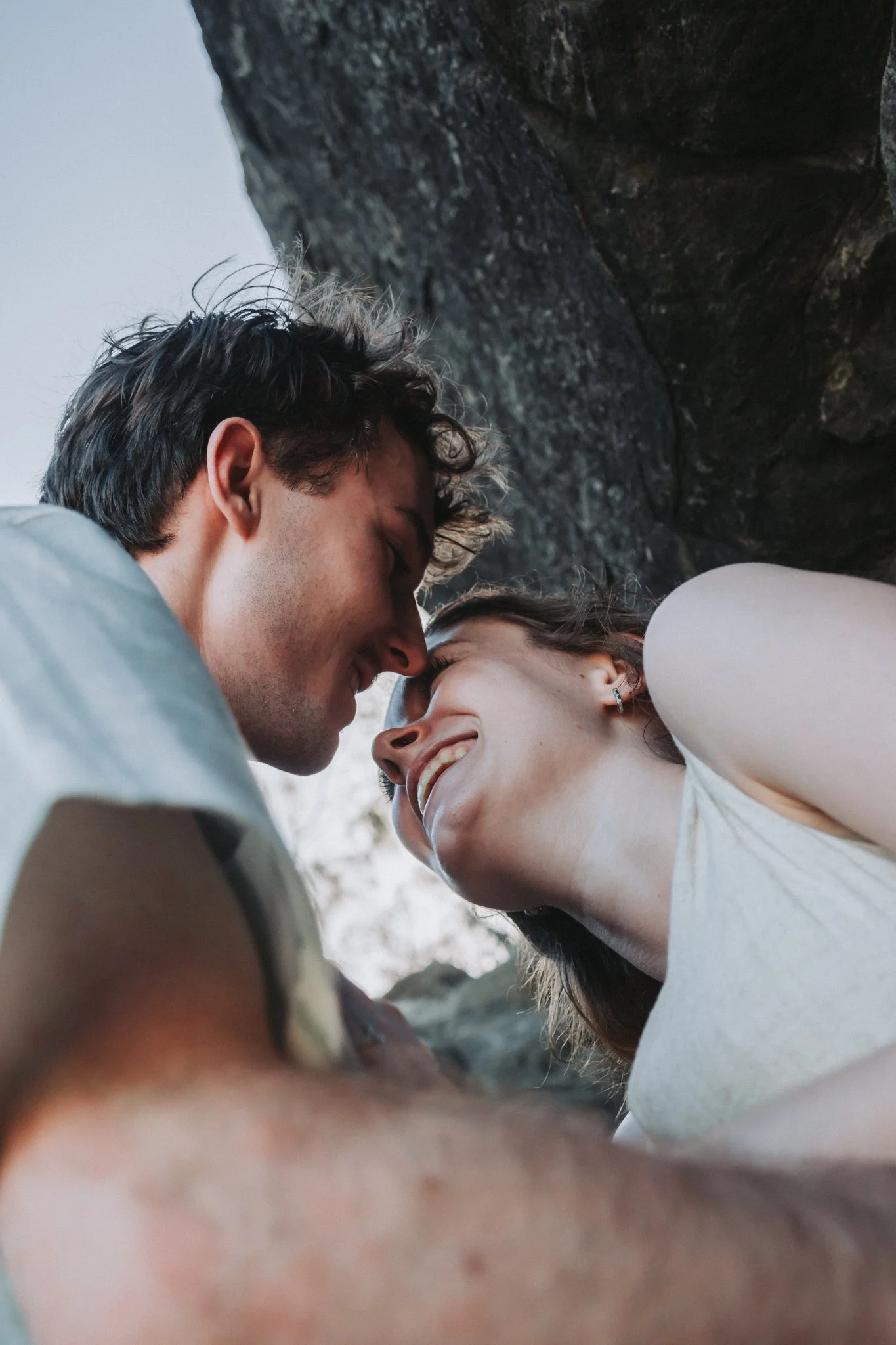 Camera pointing up to the sky throught the laughing, almost kiss of two freshly engaged lovebirds
