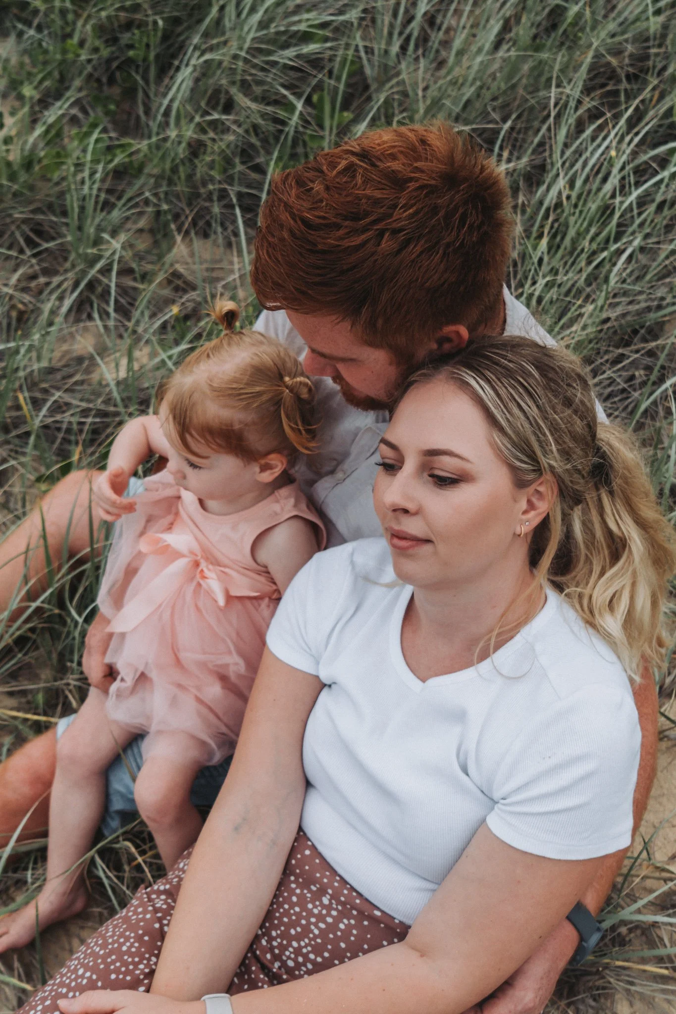 Young family of three sitting in the dunes of Kawana Beach all cuddled together