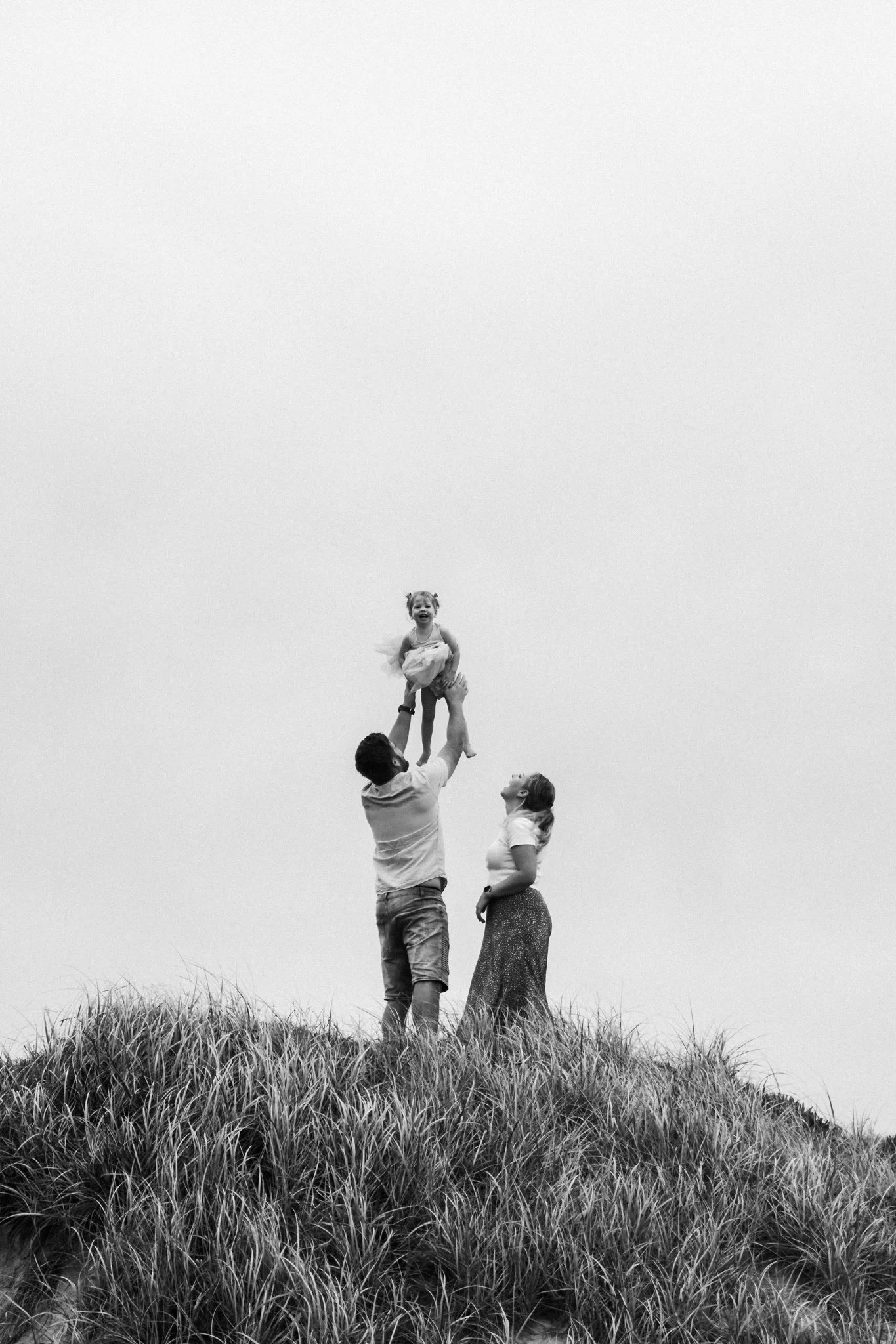 Young family of three in the sand dunes of Kawana Beach. Dad throwing his little girl high in the air and as both little girl and on-looking Mum laugh