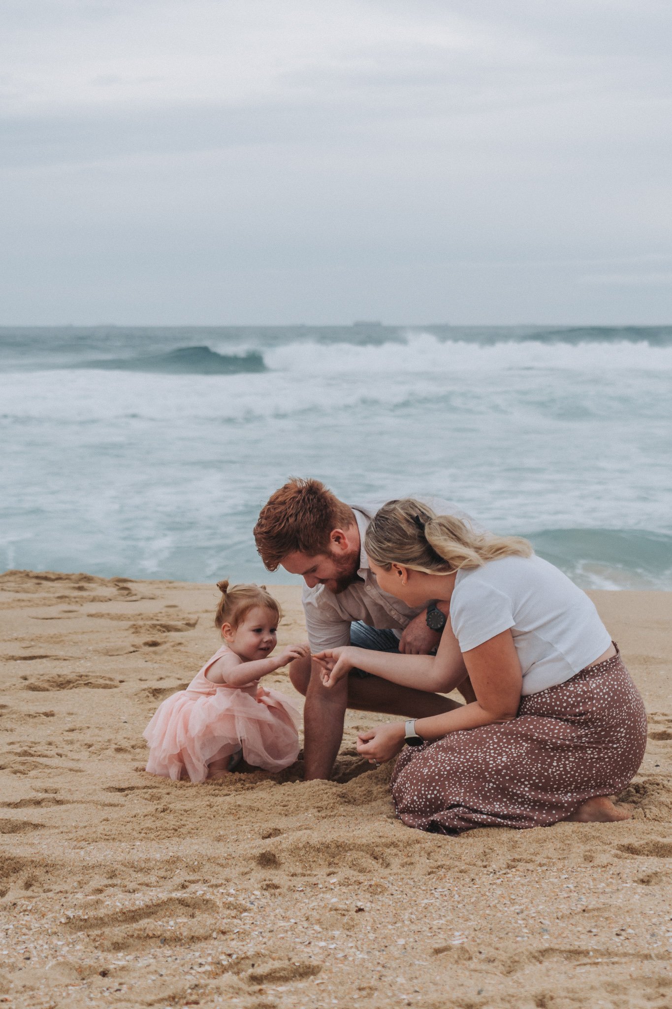 Young family of three on Kawana Beach collecting shells together