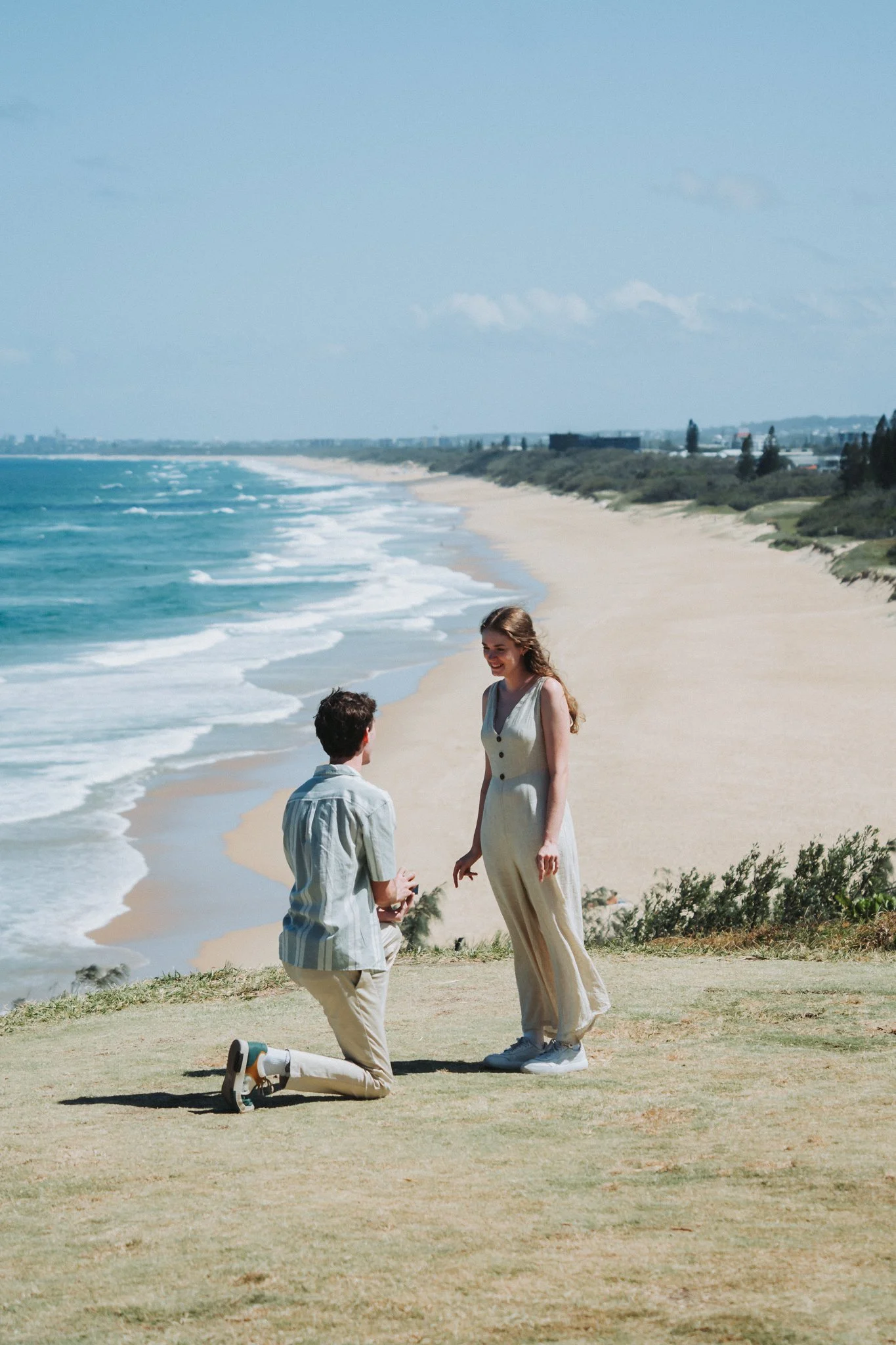 Young couples moment of proposal a top Point Cartwright lookout with long stunning views of Sunshine Coast Beach stretching out behind the bent knee, ring presented, exited moment
