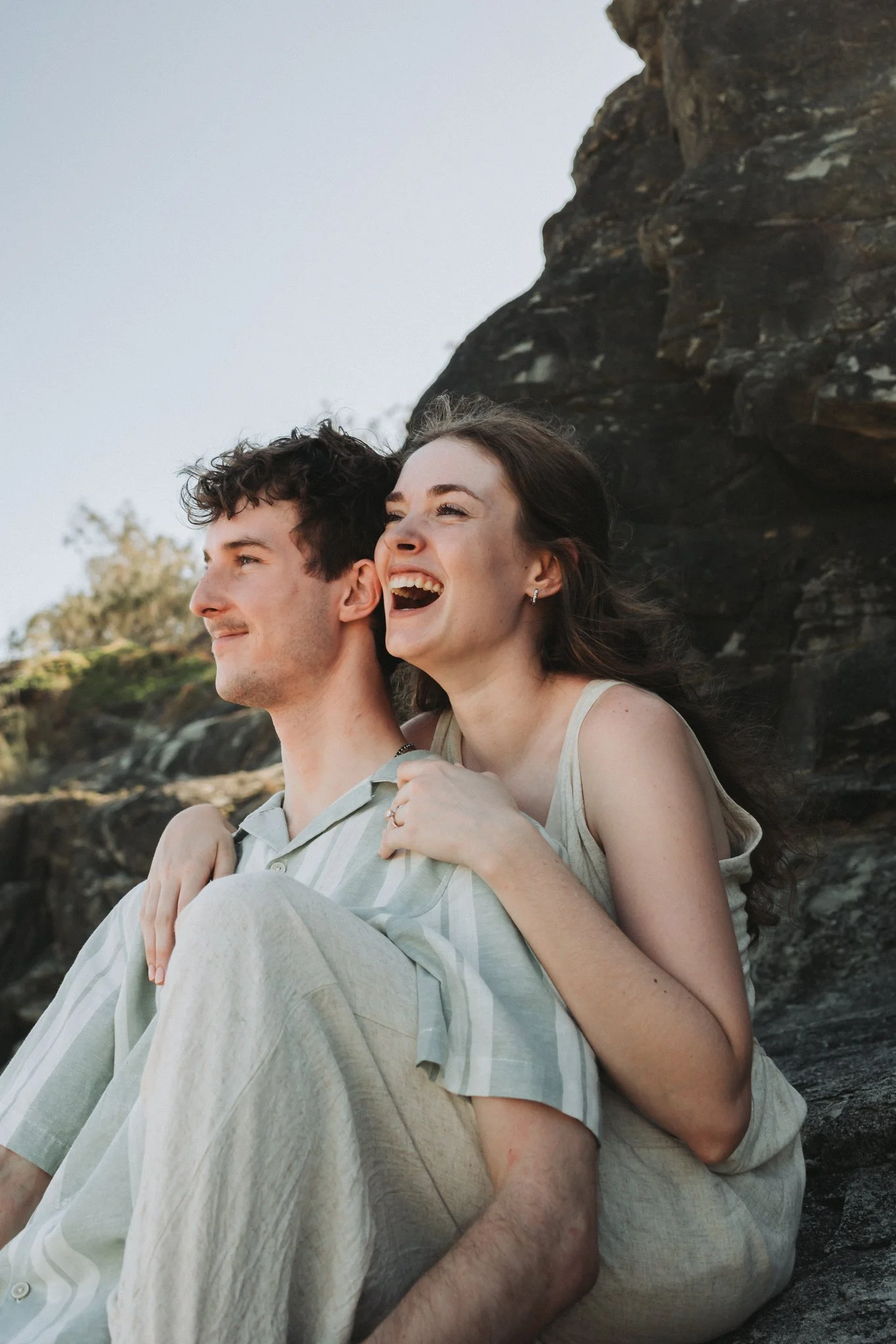 Young couple sharing cuddles and belly laughs during their engagement photo session at Point Cartwright, moments after say yes!
