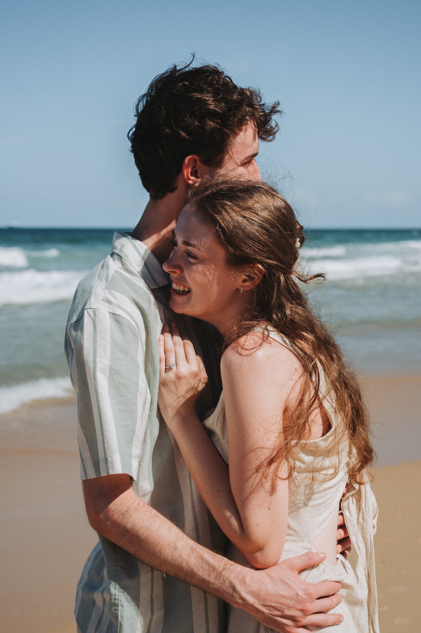 Young freshly engaged couple embrace in the sweetest cuddle, full of giggles as the iconic Sunshine Coast Beach envelopes the bliss