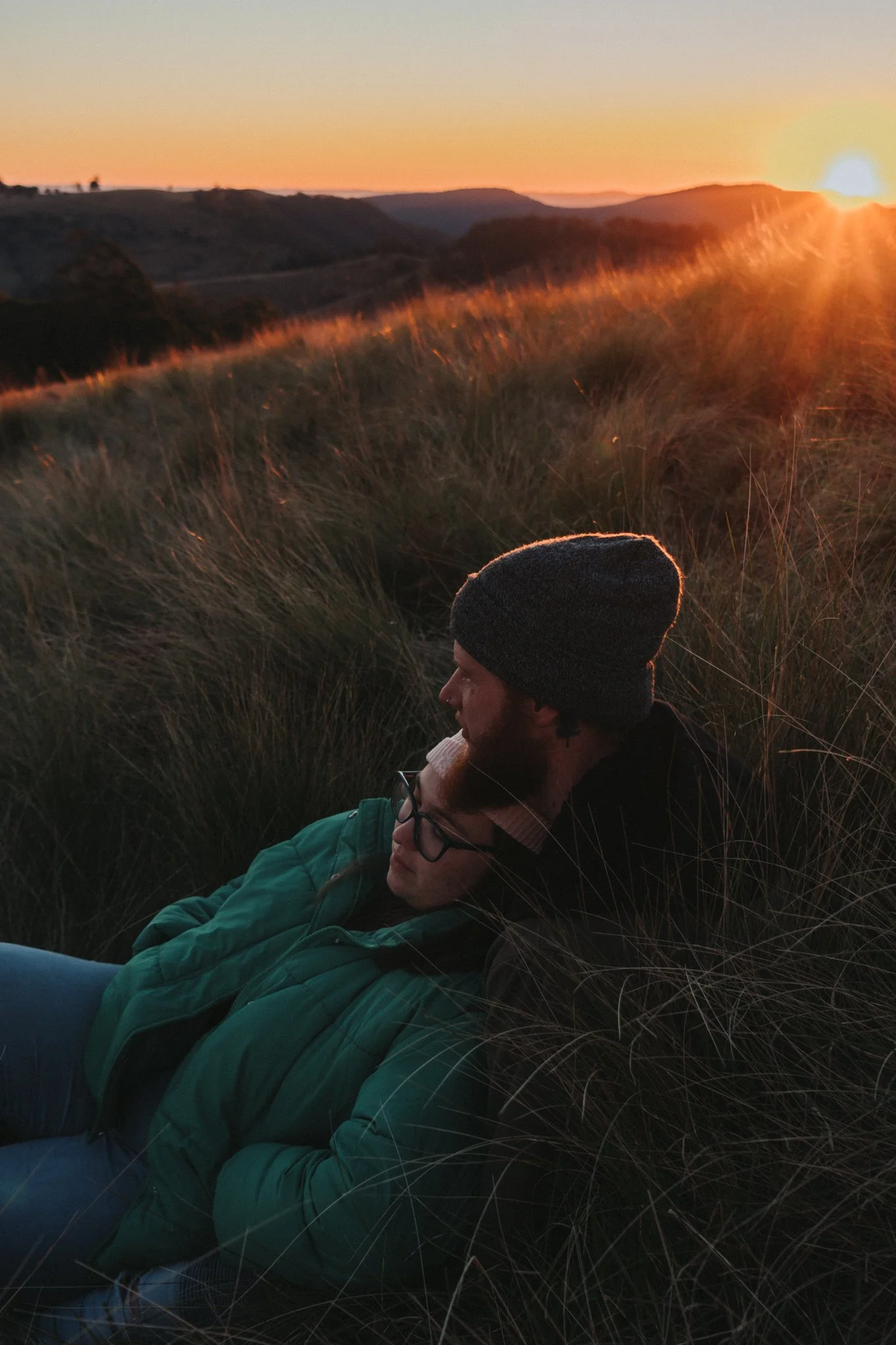 Couple couple cuddling in long grass over looking the Great Dividing Range outside Killarney at sunset