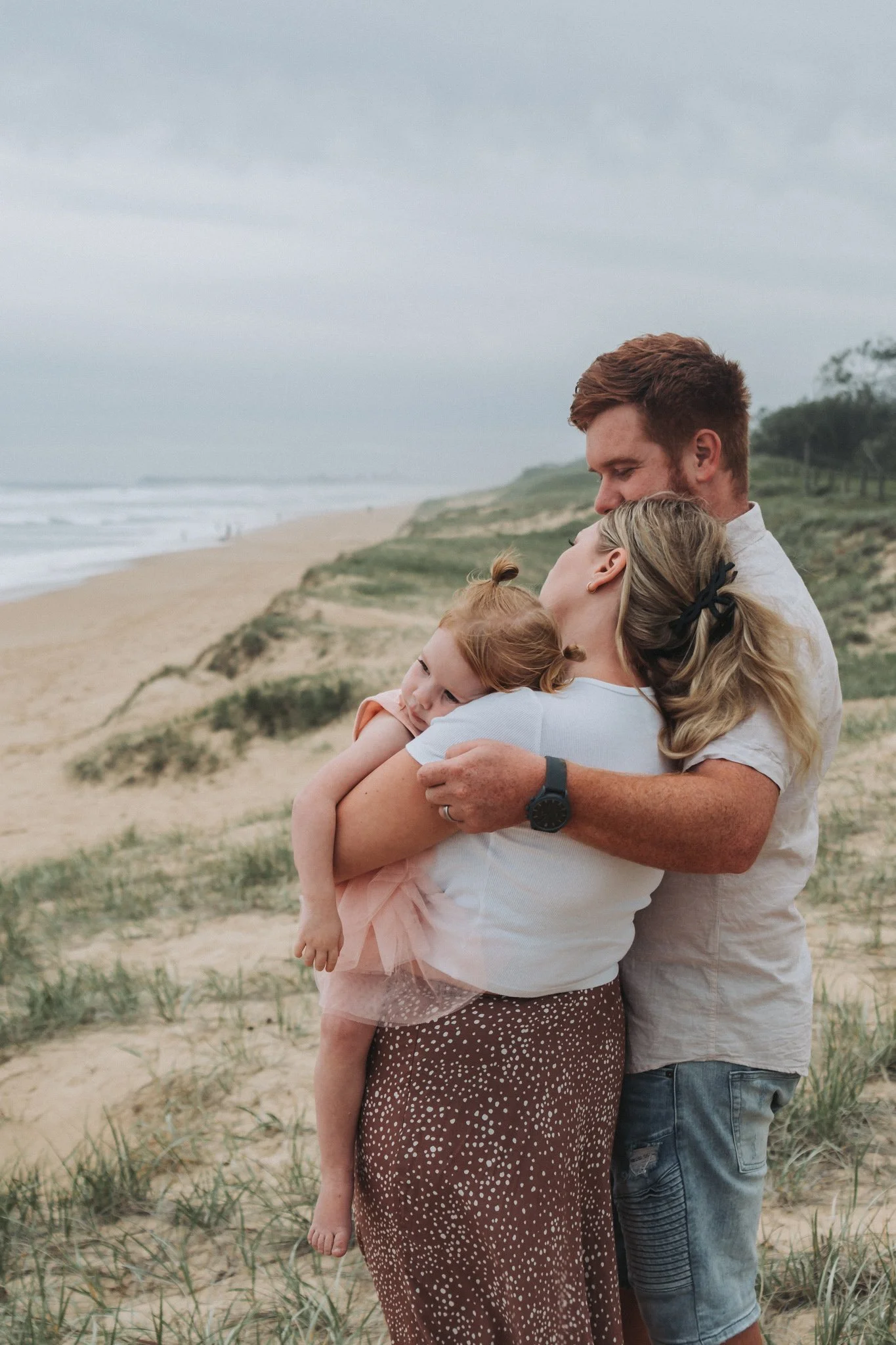 Young family of three cuddled together on Kawana Beach Sunshine Coast look out to sea