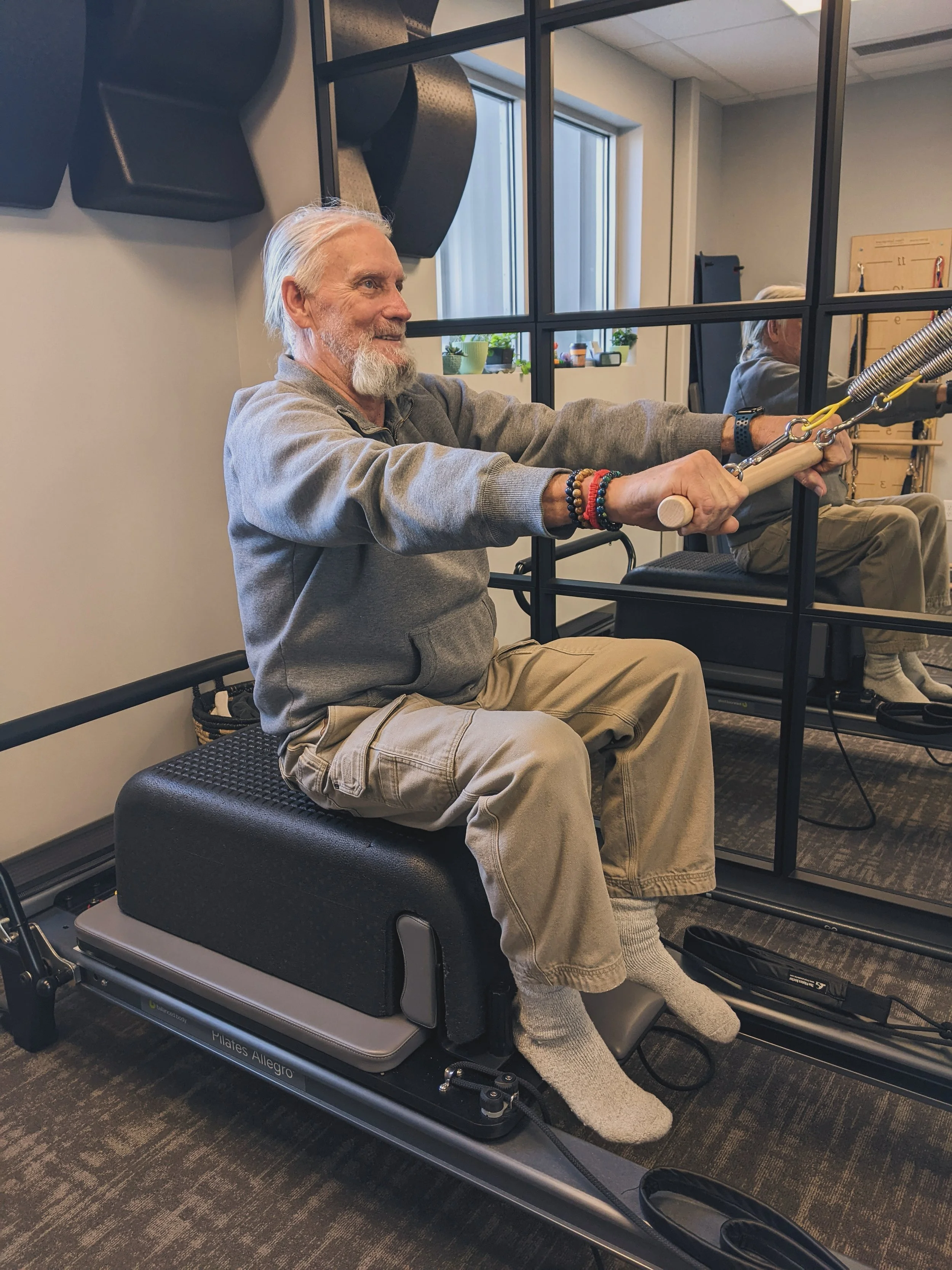 Christina's student is performing a chest pull on the reformer using metal springs. This exercise is called row and helps strength the back and open the chest.