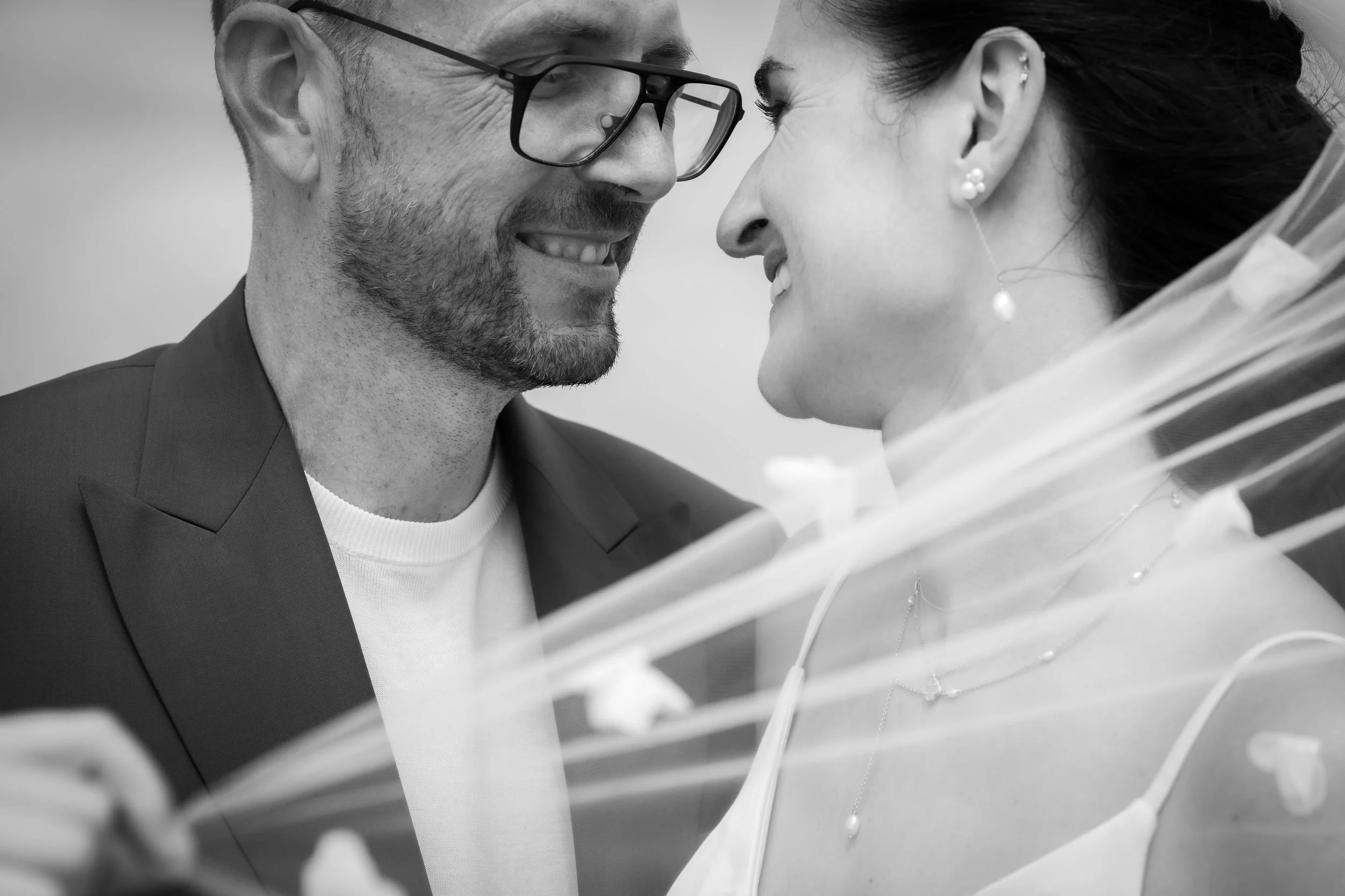 Close-up van een man en een vrouw die met hun voorhoofd tegen elkaar aanleunen, lachten en elkaar aankijken, met een witte achtergrond.