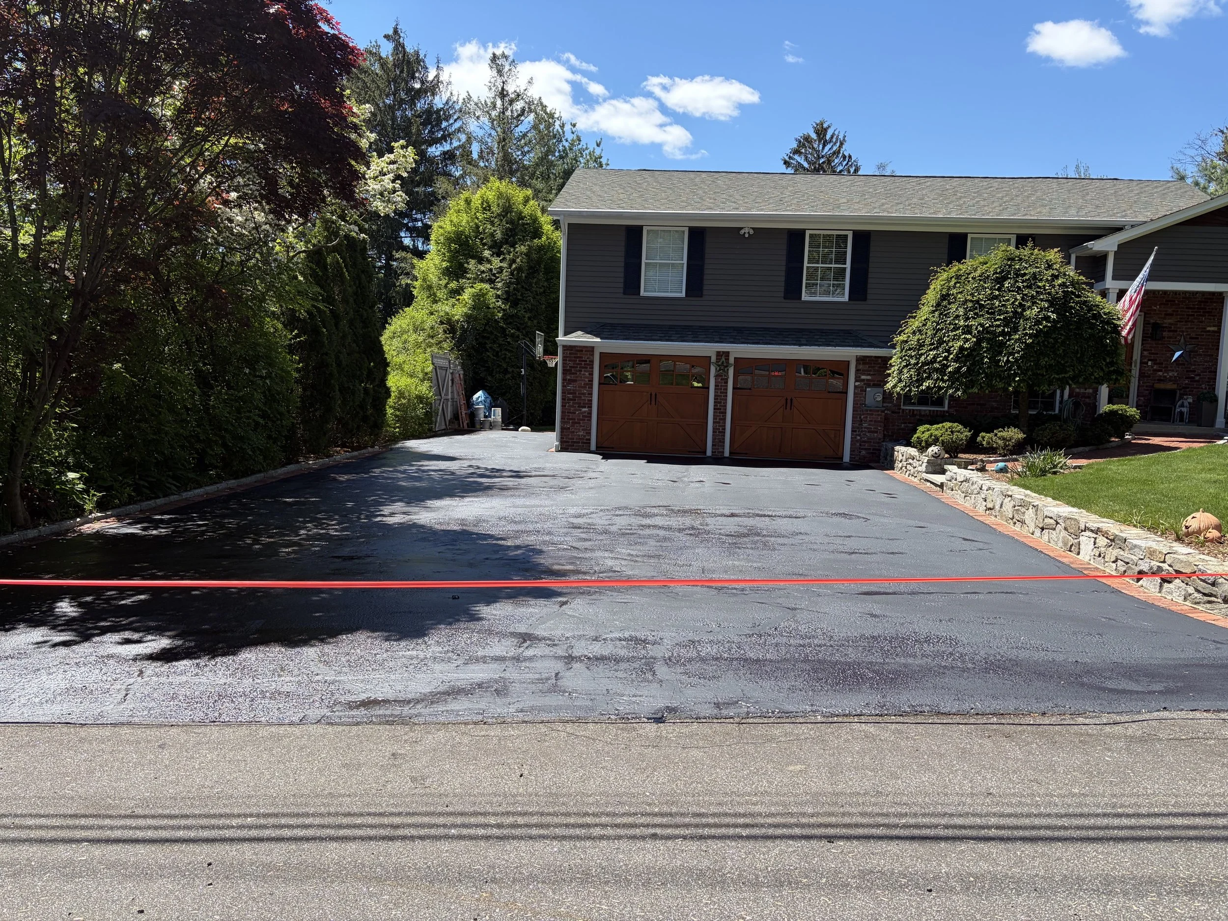 Residential driveway is seen with a freshly installed layer of asphalt sealcoating, shining under a bright sun in Fairfield, Connecticut.