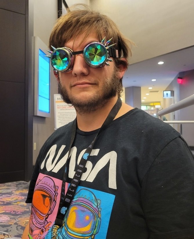 A man with goofy opaque googles and a NASA t-shirt looks at the camera.