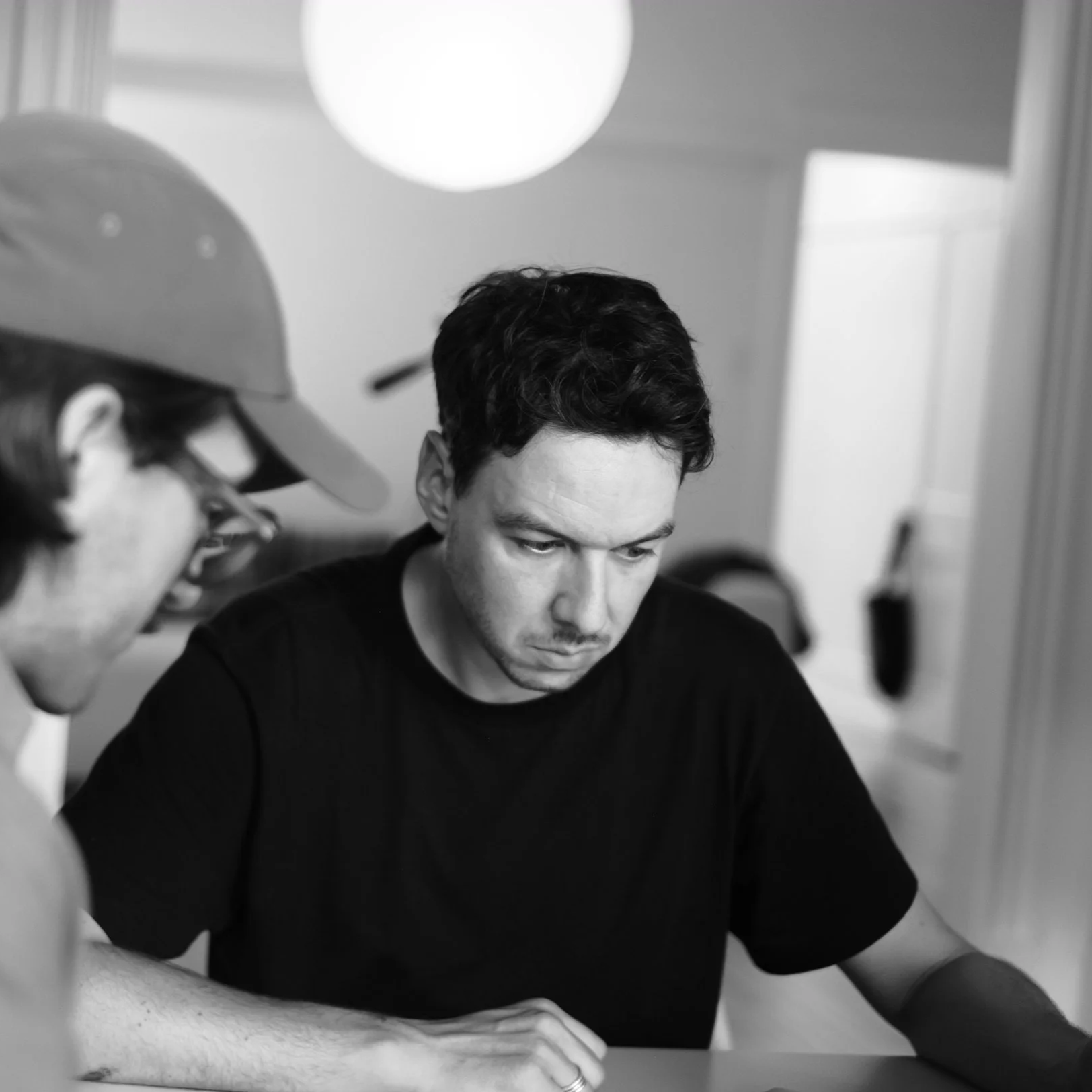 Gilbert Fortin and Guillaume Roy sitting at a table, looking at a prototype in a room with a white door and hanging lamp