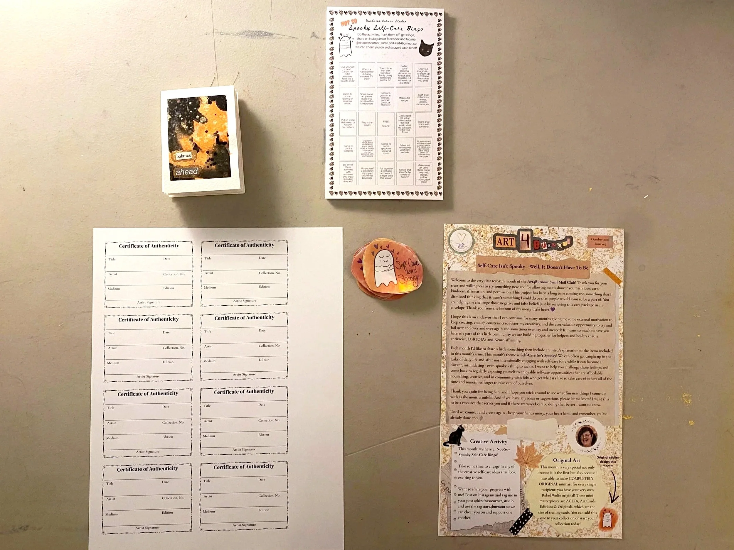 Items from the Art4Burnout monthly snail mail club including ACEOs, letter, ghost sticker, self-care bingo sheet, certificates of authenticity.