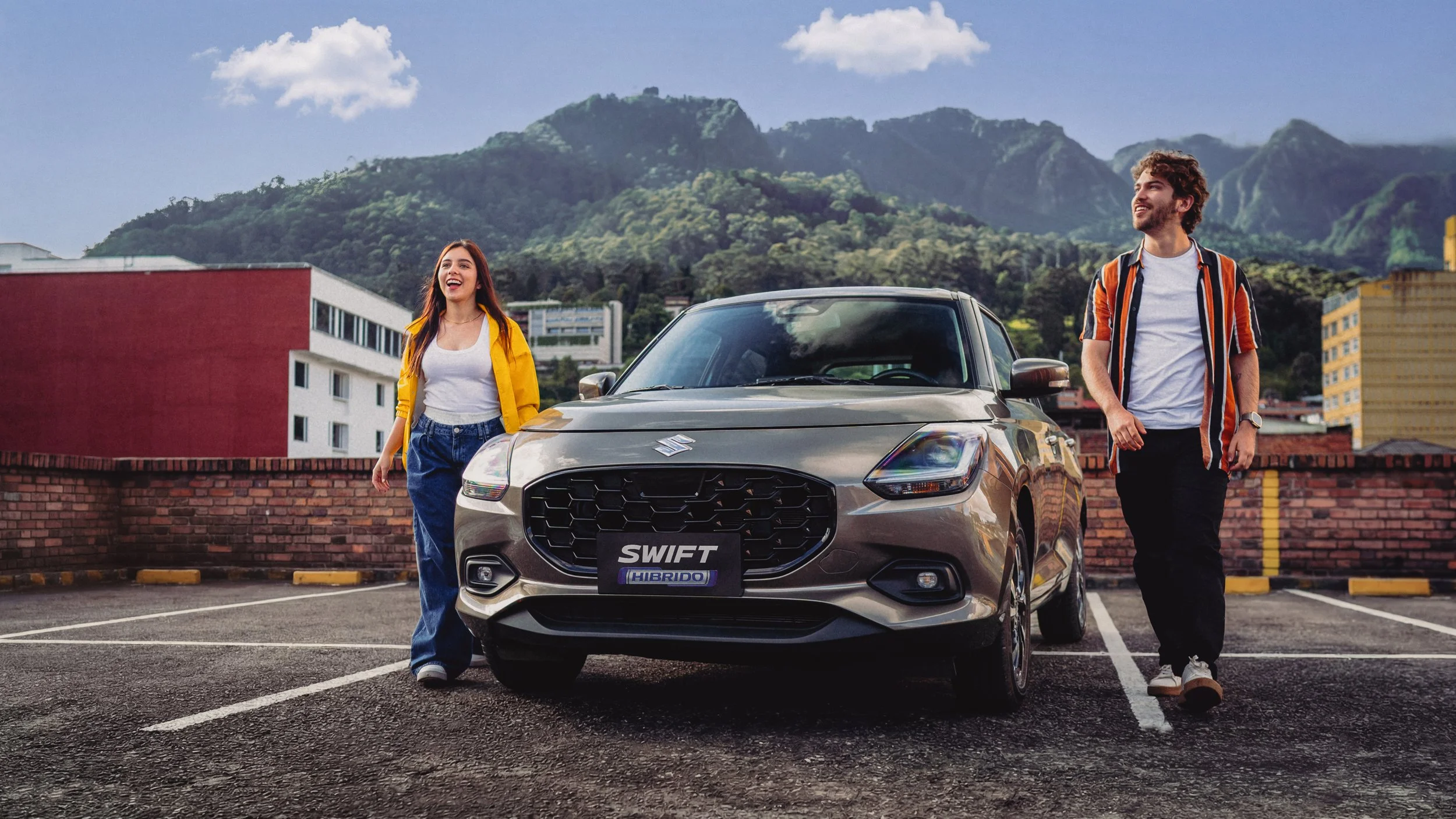 Una pareja caminando en un estacionamiento junto a un automóvil Suzuki Swift híbrido. La mujer lleva chaqueta amarilla y pantalones de mezclilla, mientras que el hombre usa una camiseta blanca y camisa de rayas con pantalones oscuros. Detrás hay mont