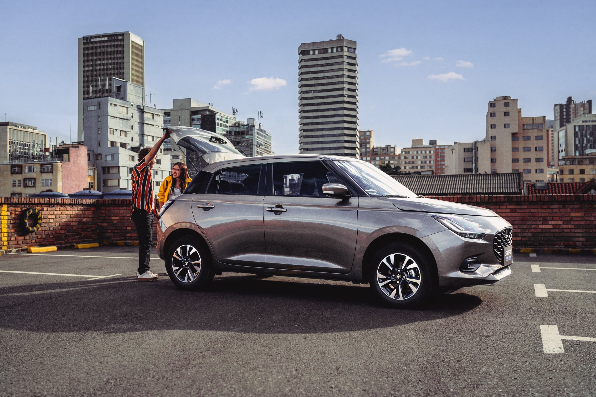 Dos personas cargando maletas en un cocheplateado en una azotea con skyline urbano de edificios