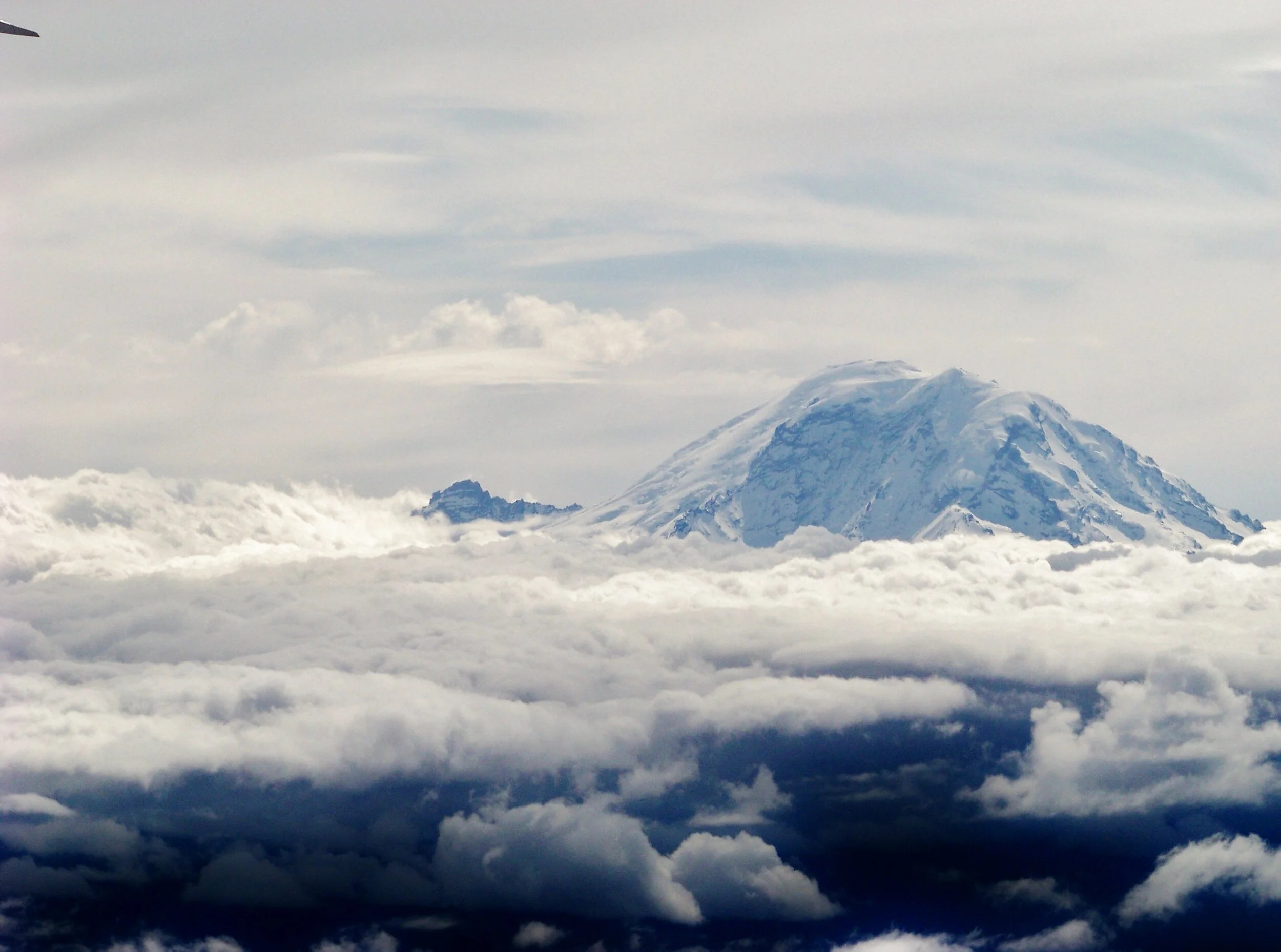 Snow-covered mountain peak rising above thick clouds in the sky.