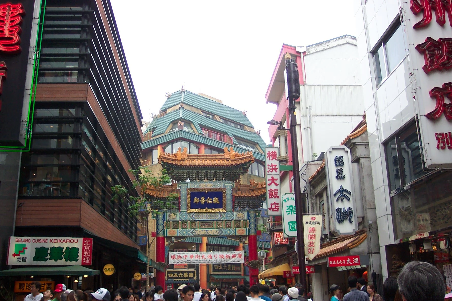 Crowd walking through a busy Chinatown street with traditional Chinese gate and pagoda-style buildings in the background.