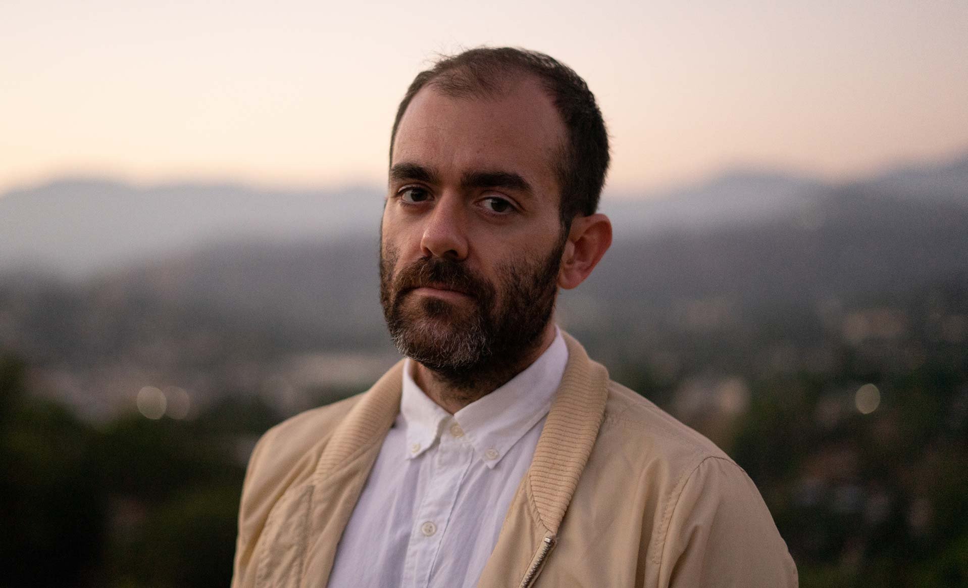 Artist and director Sean David Christensen smiling outside on a mountaintop.