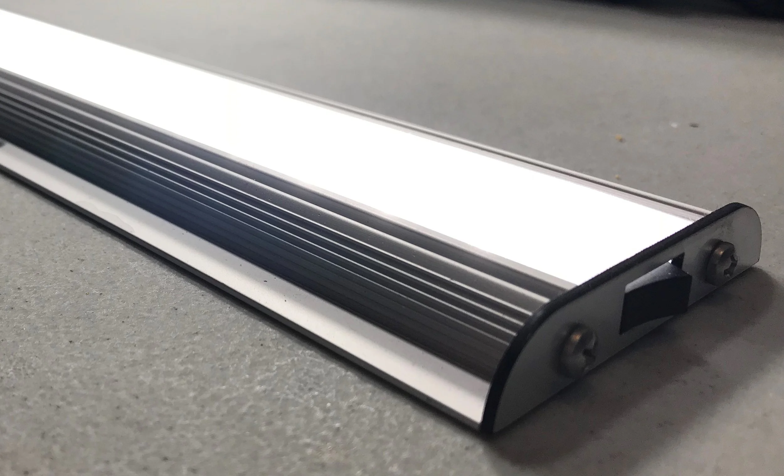 The H2 surface mount linear LED light is 12 inches long and has a rocker switch on the end cap. It is anodized in a metallic color, which makes it look sleek and modern.