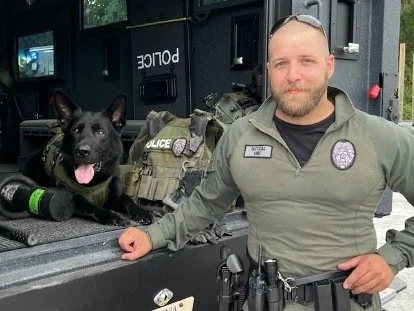 An LPD officer with a K-9 partner beside a police tactical vehicle.