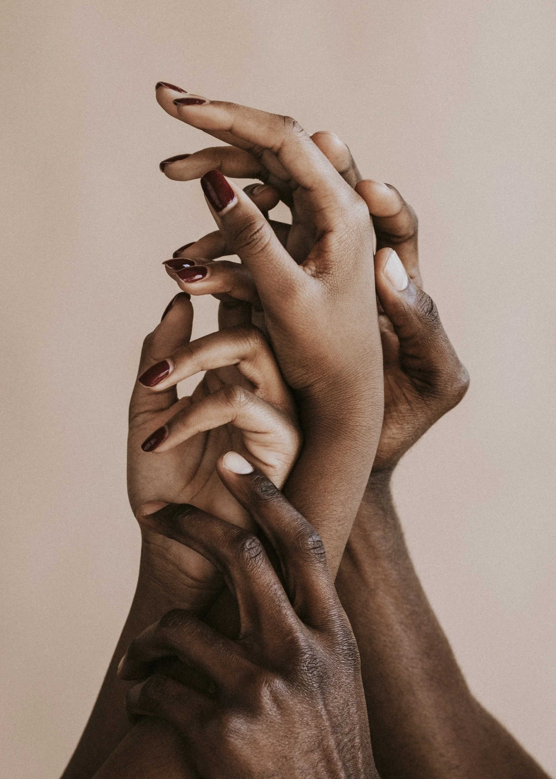 Multiple hands of different skin tones intertwined against a plain light background.