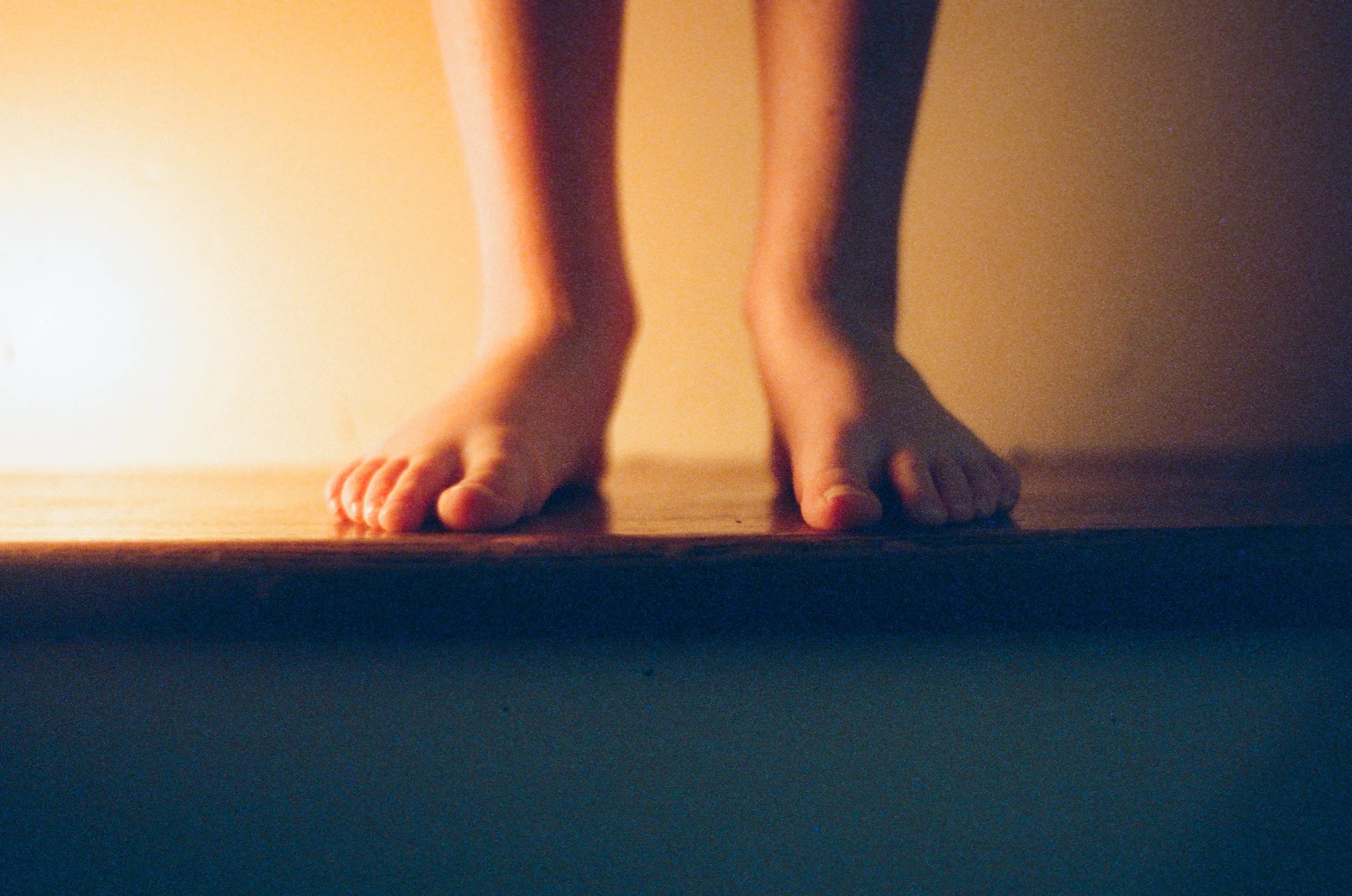 Close-up of a person's feet standing on a wooden floor, with the background dimly lit.