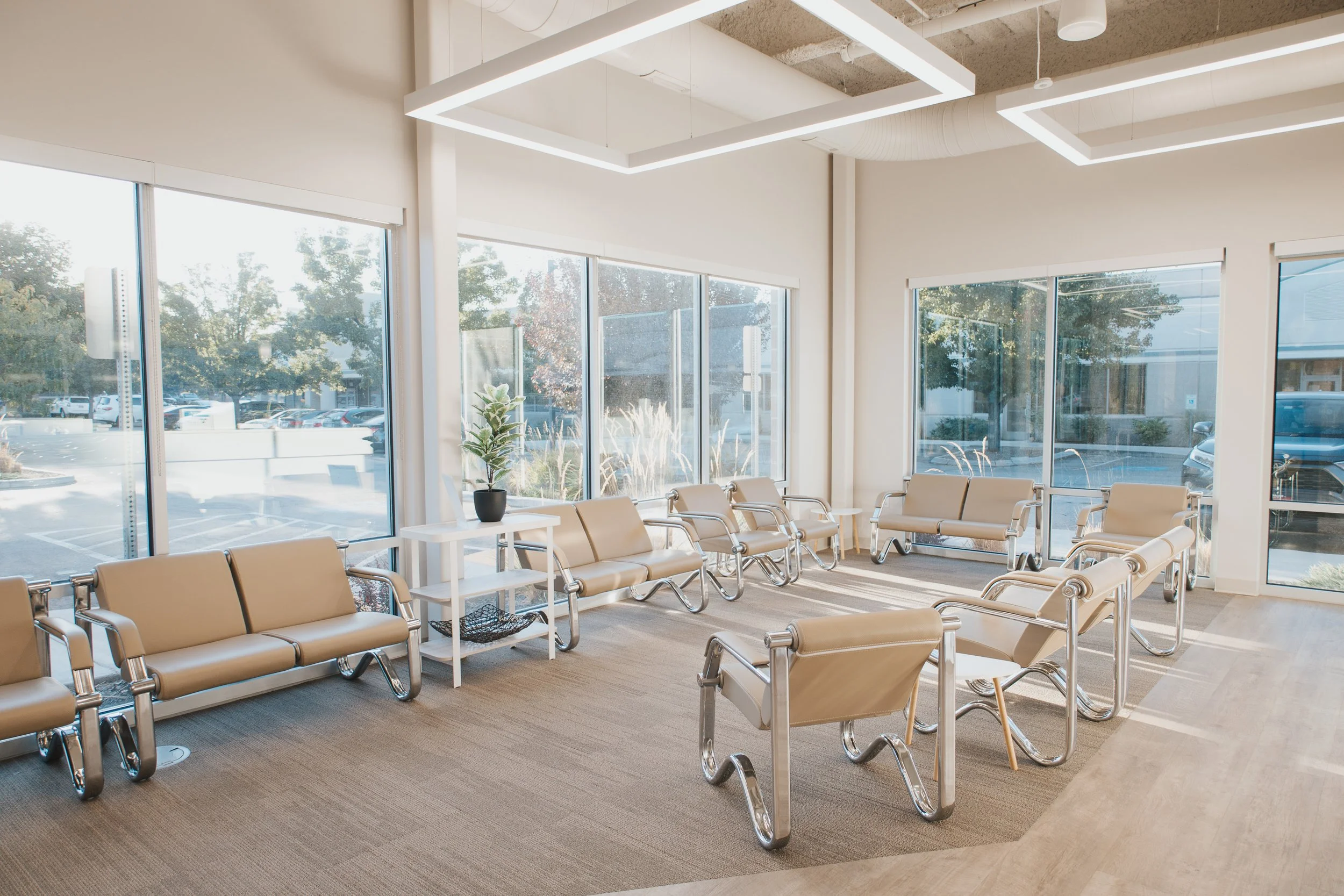 Empty waiting room with beige chairs, large windows, and modern ceiling lights in a medical or office building.