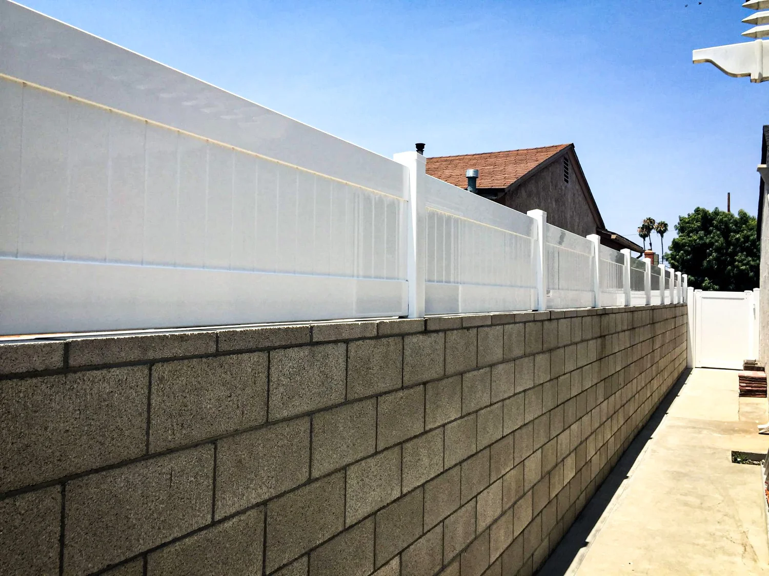 White vinyl wall topper installed on top of a block wall along a side yard