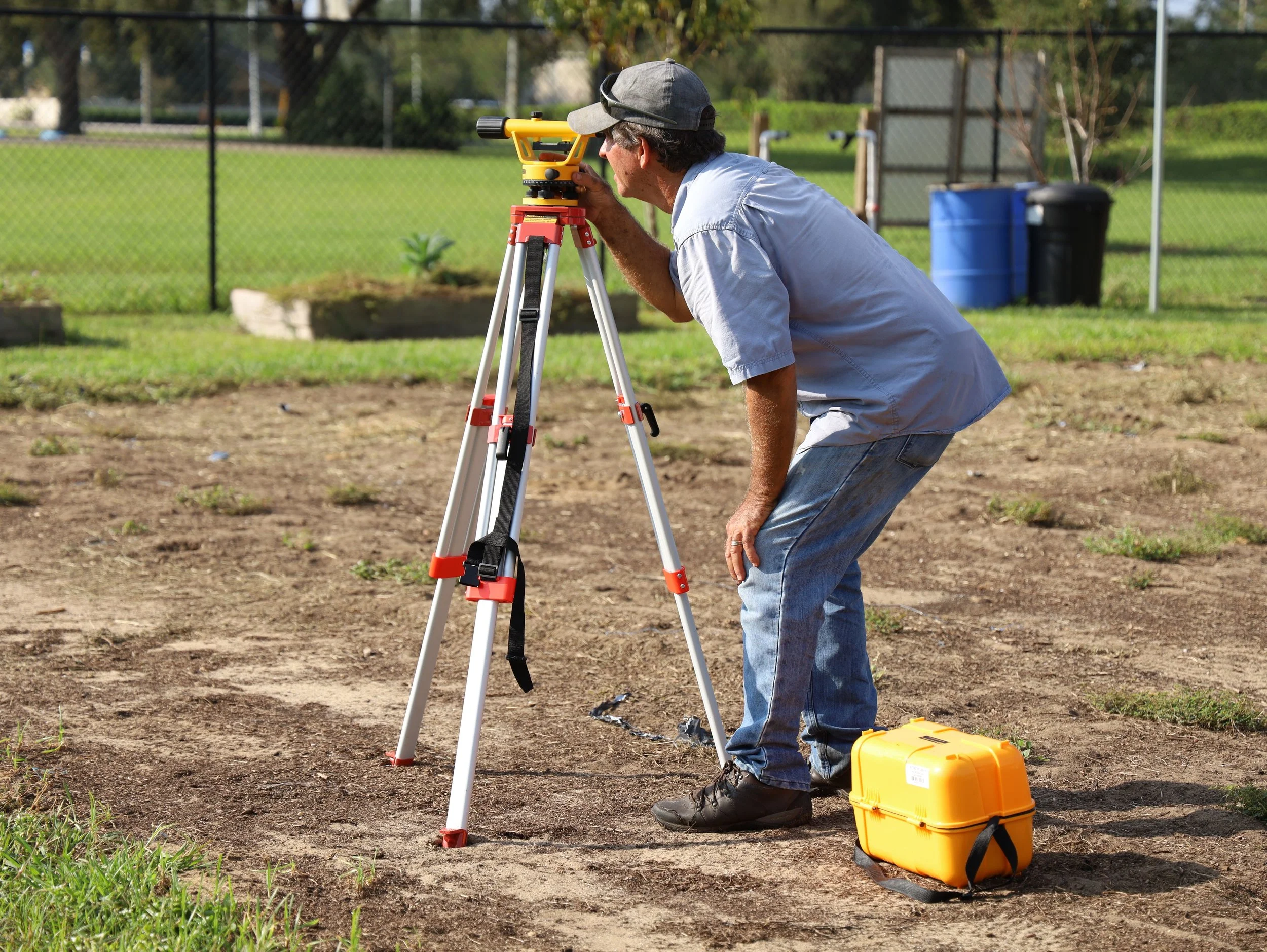 Licensed land surveyor using a tripod instrument to confirm a property boundary line before a fence installation