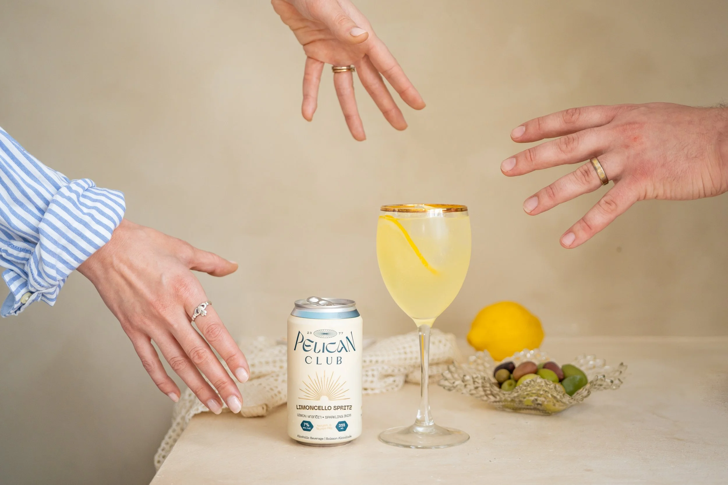 Product photo for Pelican Club. Three hands are reaching for a Peli Limoncello Spritz can and poured glass