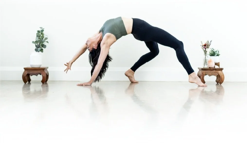 A woman performing yoga in a plank pose in a bright room with minimal decor, including small tables with plants on either side.