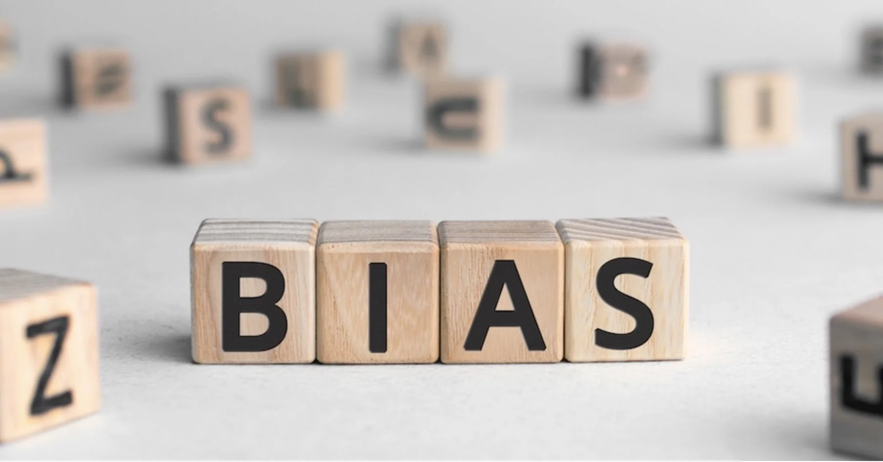 Wooden blocks spelling 'BIAS' on a plain surface, with other scattered blocks with letters and numbers blurred in the background.
