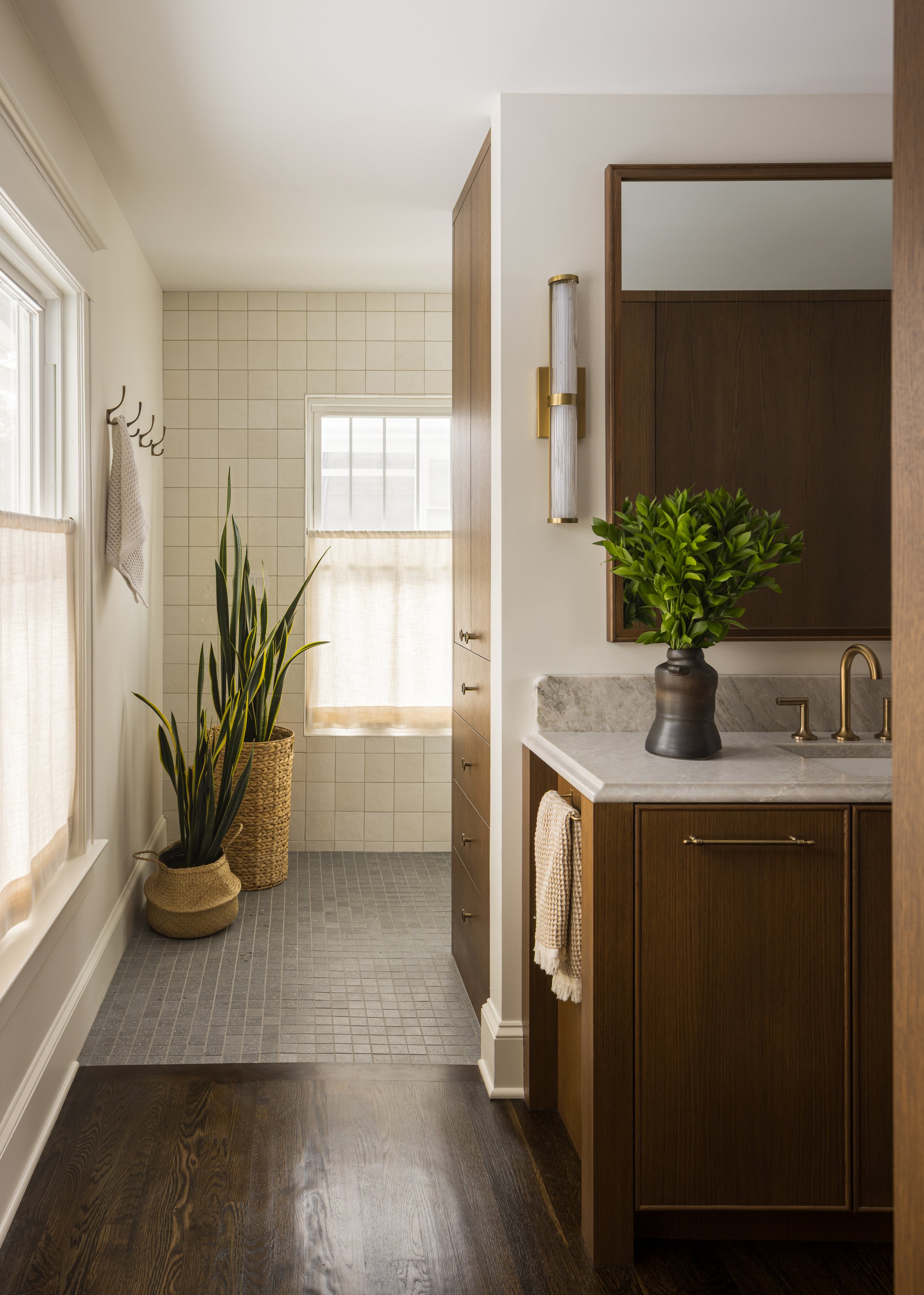Historic Brookside Neighborhood shirtwaste home remodel of a primary bathroom. Antique cabinet details in a walnut tone with Ogee edge quartzite countertop and curved backsplash. Mirror matches cabinets, linen closet outside of wet room. Simple windo