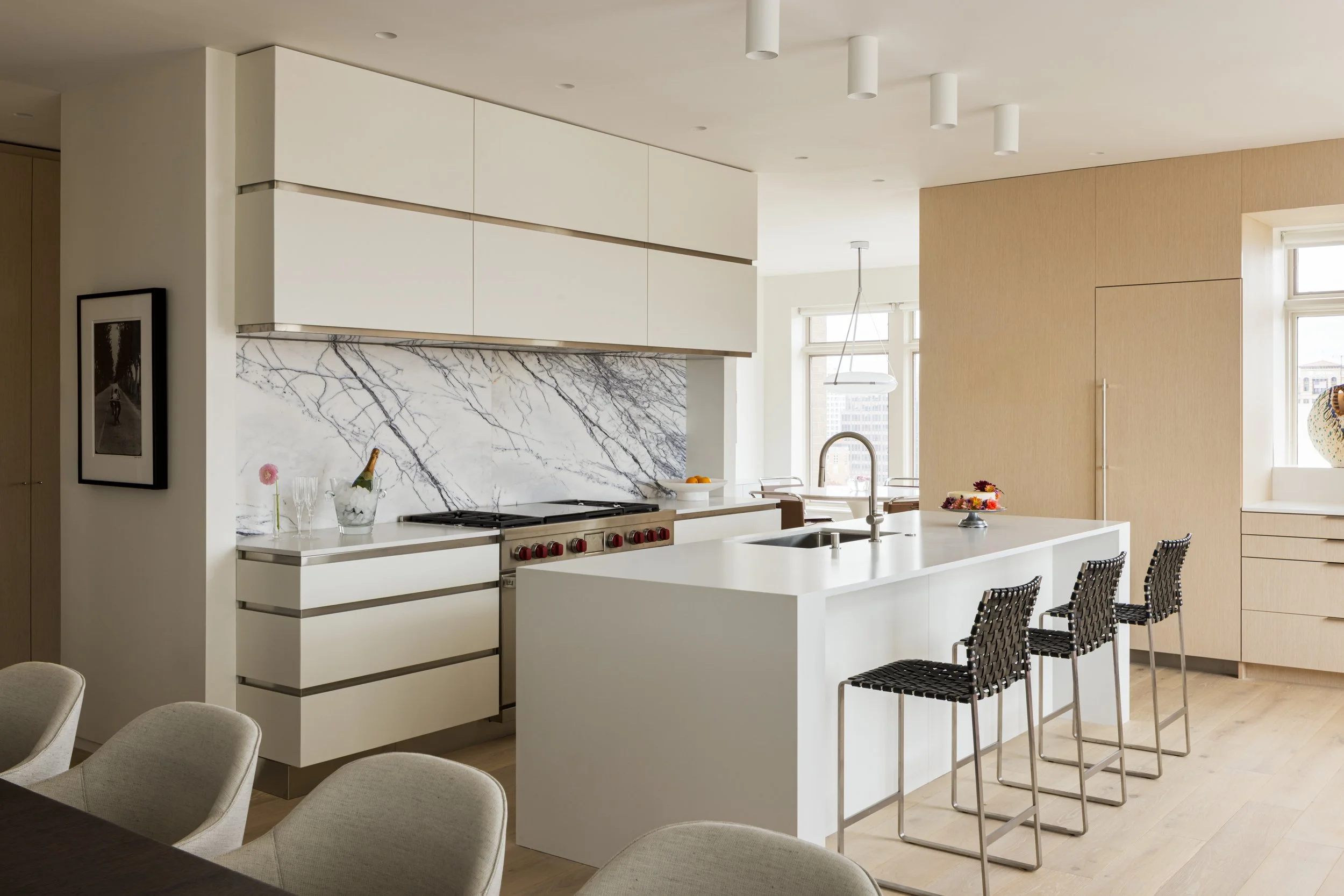 Modern kitchen with white cabinets, marble backsplash, and a large island with black barstools.