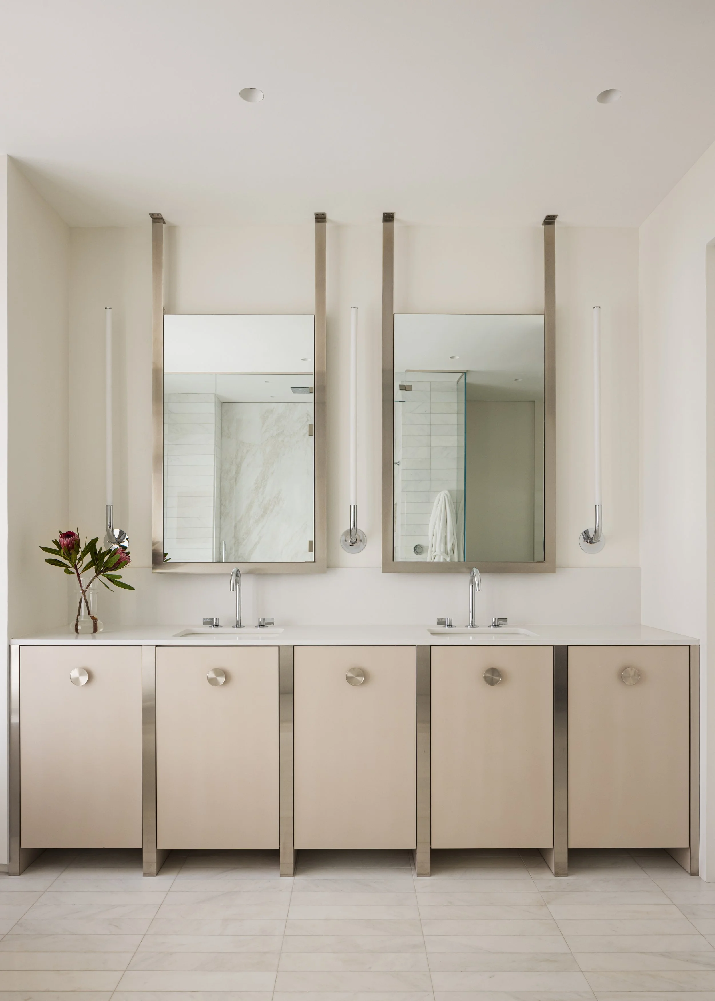 Bathroom vanity with two sinks, two large mirrors, and a beige cabinet with a white countertop.