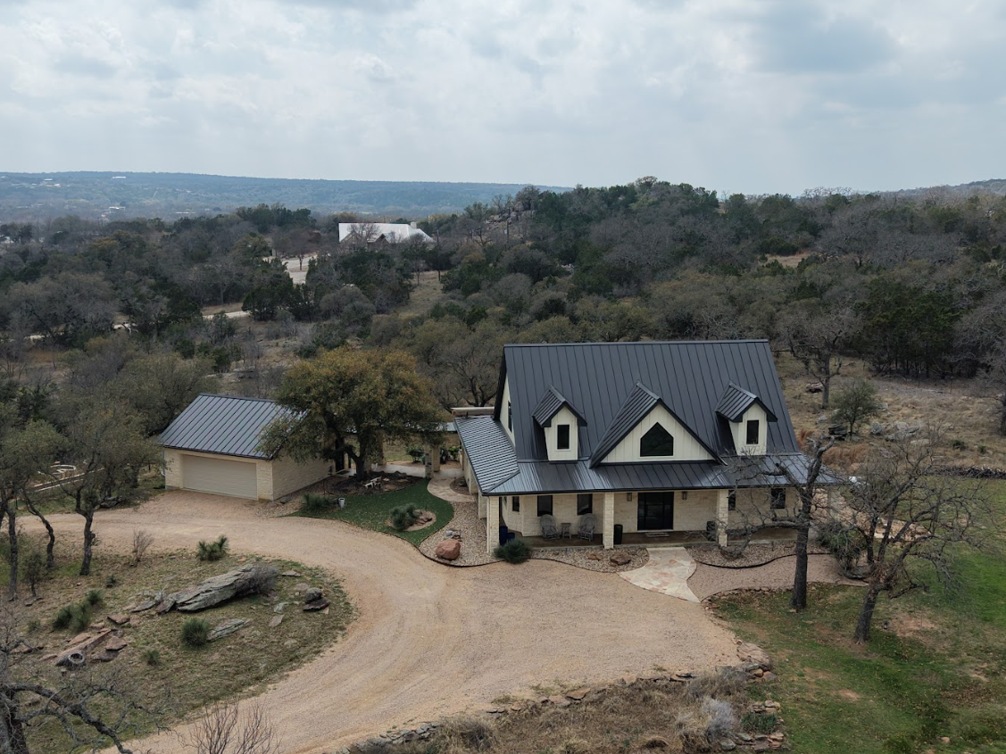 Aerial view of a custom-built Hill Country home in Burnet, featuring a modern metal roof, natural stone masonry, and a meticulously cleared lot by Owens Contracting.