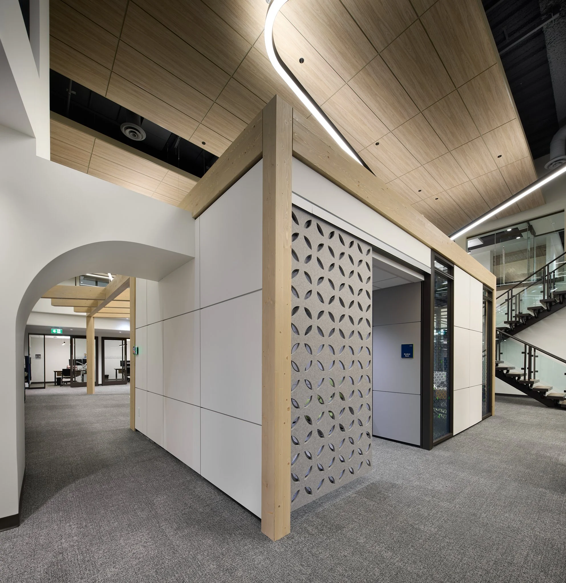 Modern office and architectural design of an interior with a wooden ceiling, white walls, a decorative partition with circular cutouts, a staircase with glass railing, and a small meeting room with sliding doors