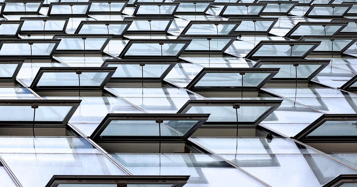Multiple glass windows of a modern building with some windows open, viewed from below.