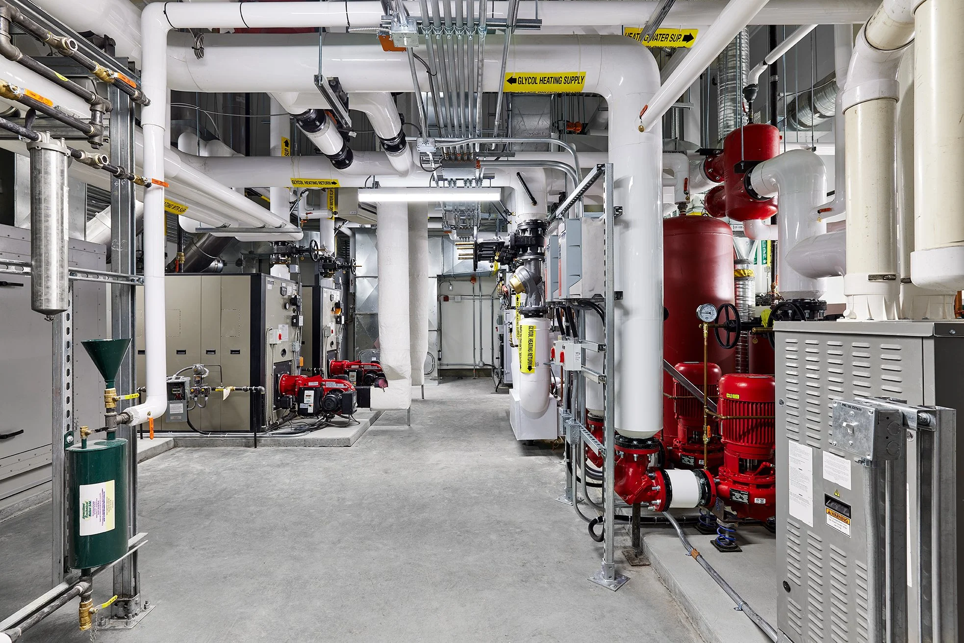 Interior of an industrial mechanical room with white and red pipes, valves, gauges, and machinery, used for heating, cooling, or fire suppression systems.
