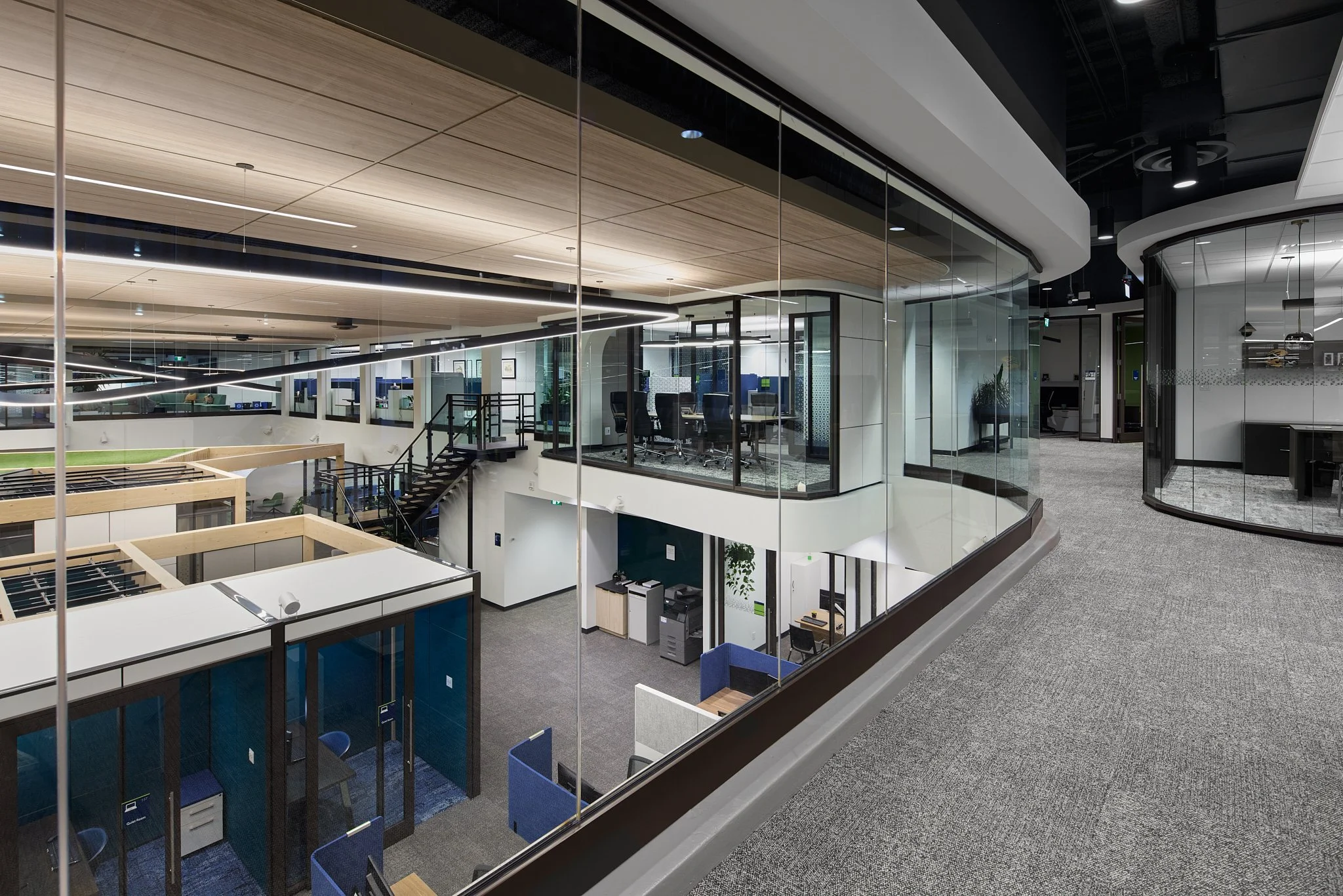 Modern office interior with glass walls, open workspace, and meeting rooms, featuring wooden ceilings and contemporary furniture.