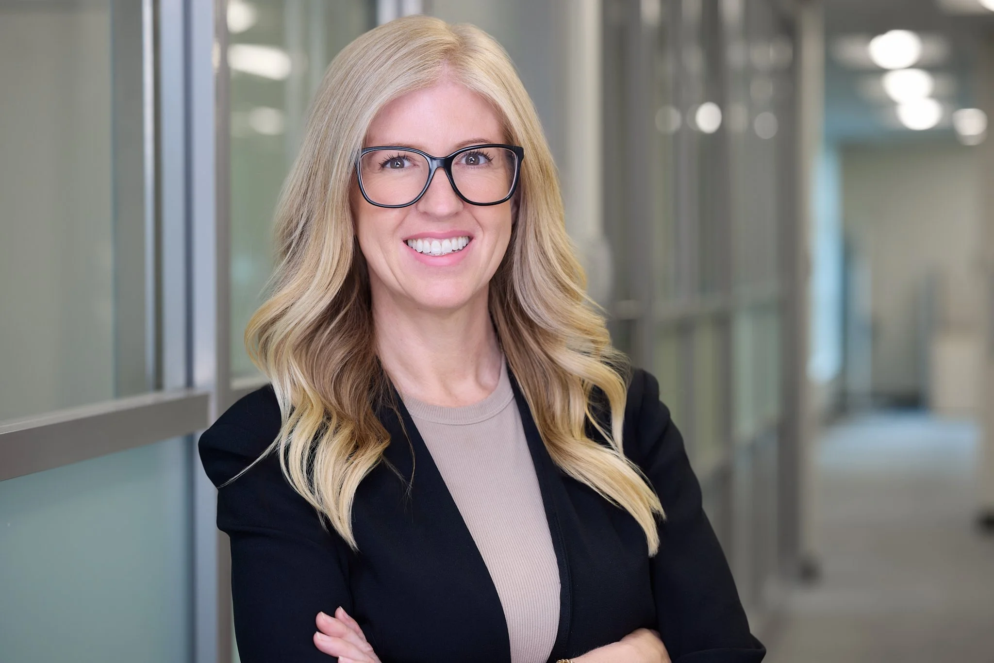 Corporate executive headshot of a woman standing with arms crossed with office hall in background