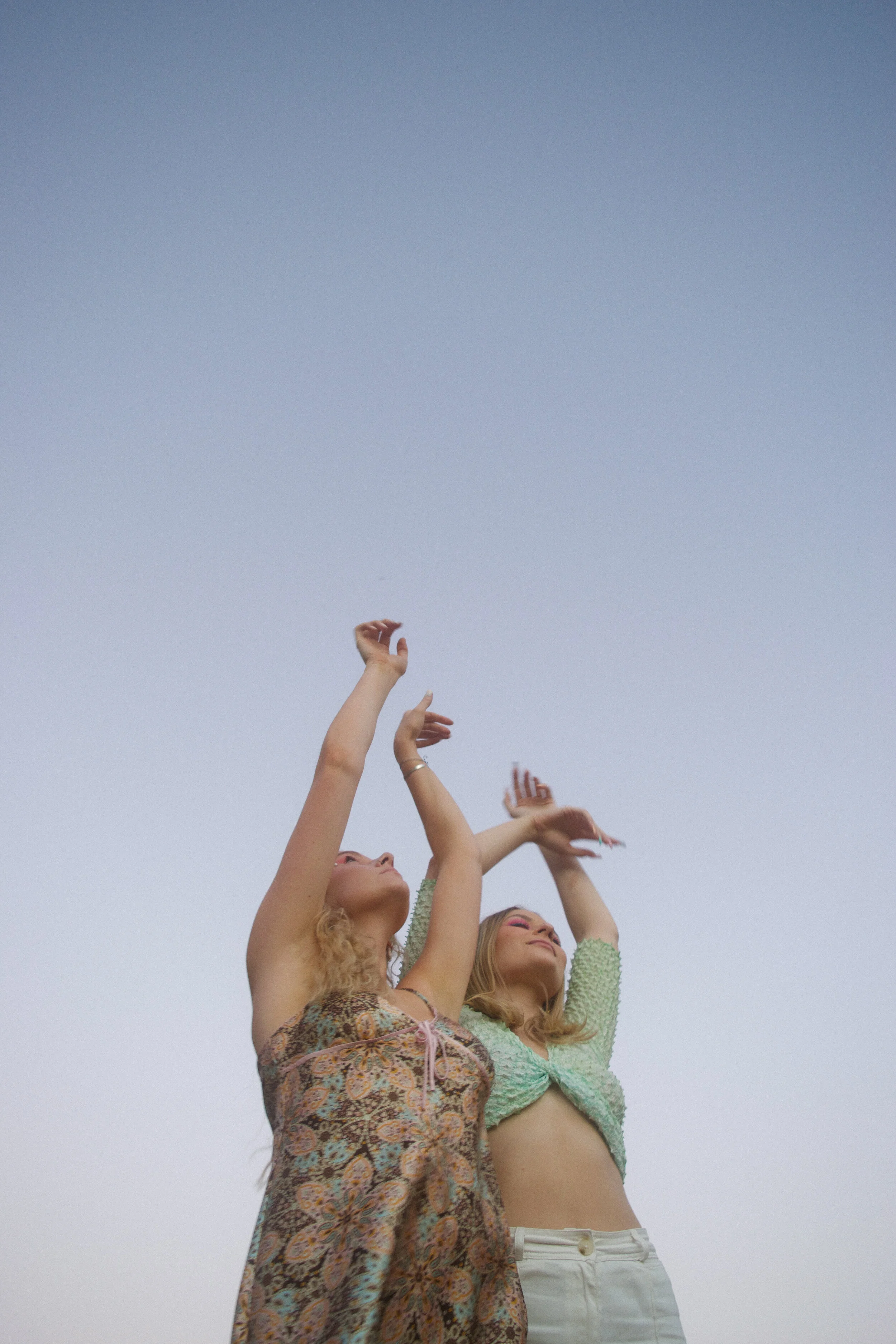 Three women with arms raised, standing against a clear sky, celebrating and smiling.
